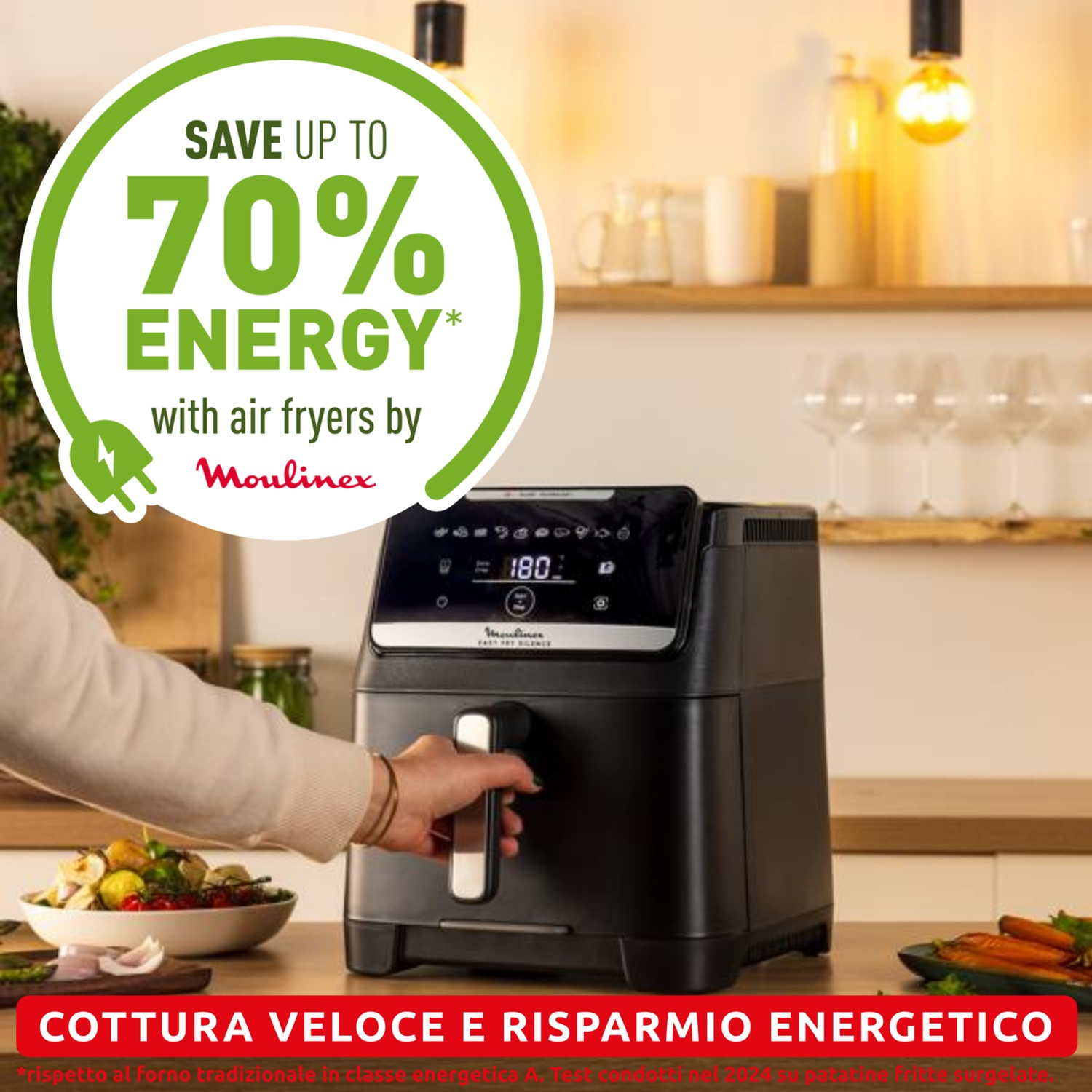 Una donna tiene in mano una friggitrice ad aria. Un cerchio verde dice 'Risparmia fino al 70% di energia'. Verdure e calici sullo sfondo.