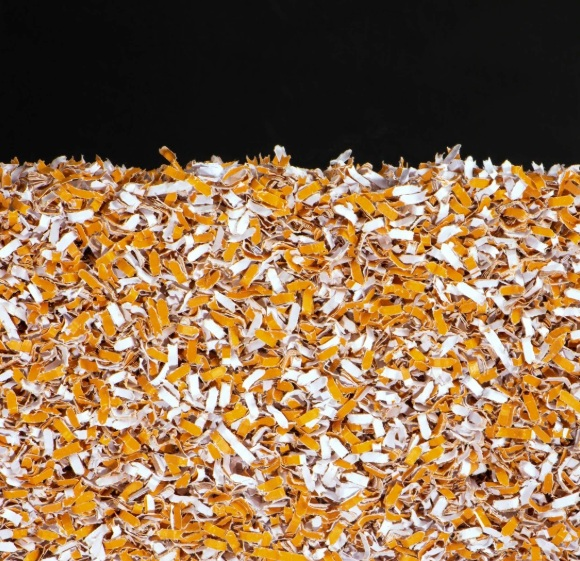 Zbliżenie pociętego papieru w kolorach pomarańczowym i białym na czarnym tle. Papier jest gęsto upakowany.