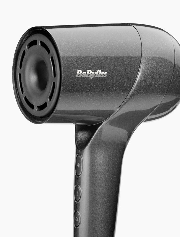 Pokazano ciemnoszarą suszarkę do włosów Babyliss. Ma okrągłą głowicę z otworem wentylacyjnym, uchwyt z przyciskami. Tło jest białe.