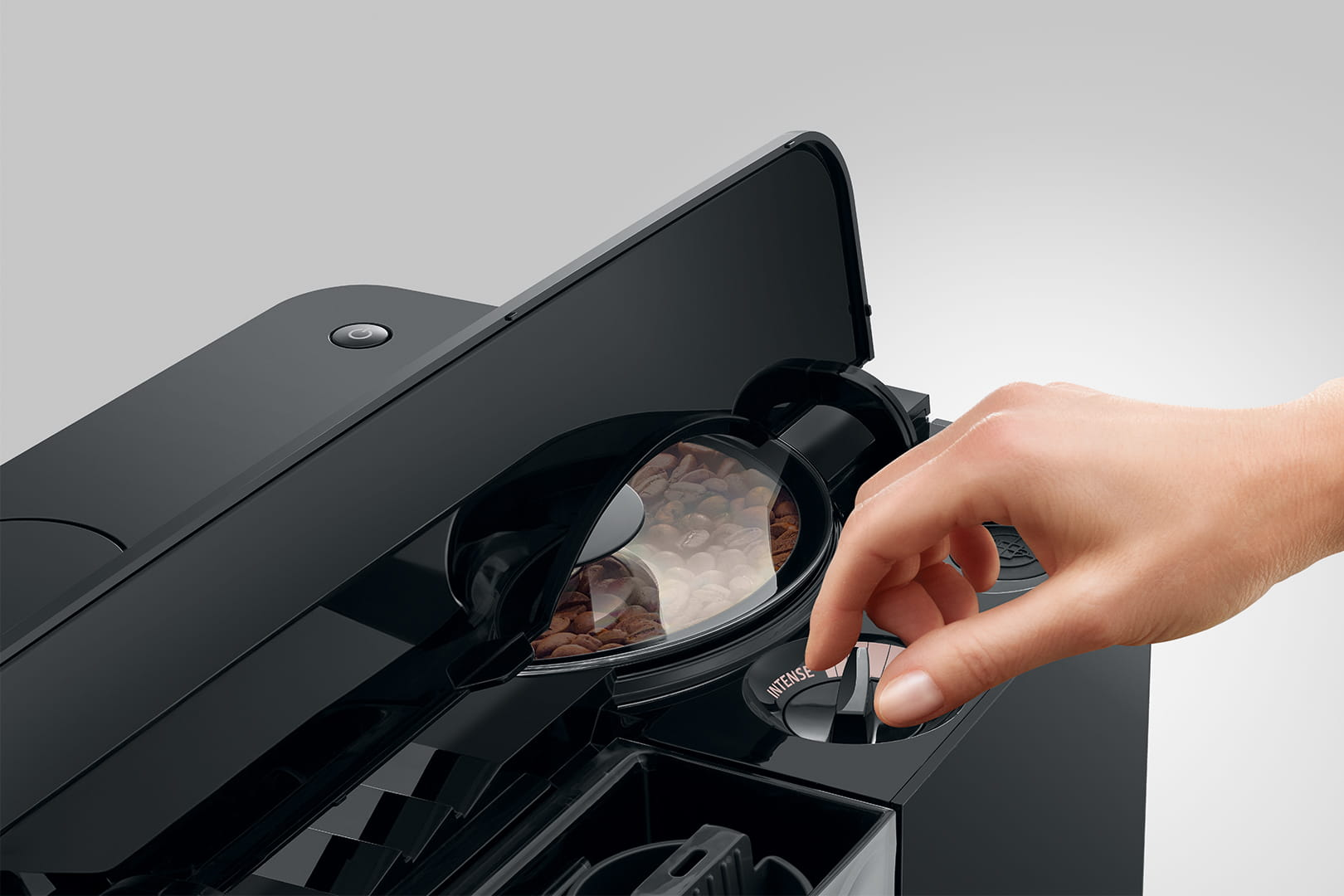 Ręka reguluje ustawienia ekspresu do kawy. Ziarna kawy widoczne w pojemniku. Maszyna jest czarna.