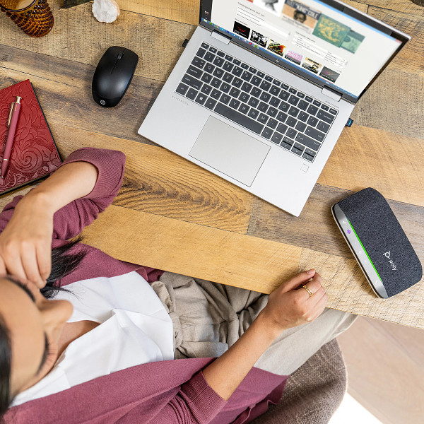 Eine Person sitzt an einem Holzschreibtisch mit Laptop, Maus und Notizbuch. Rechts befindet sich ein Gerät mit grünem Licht.
