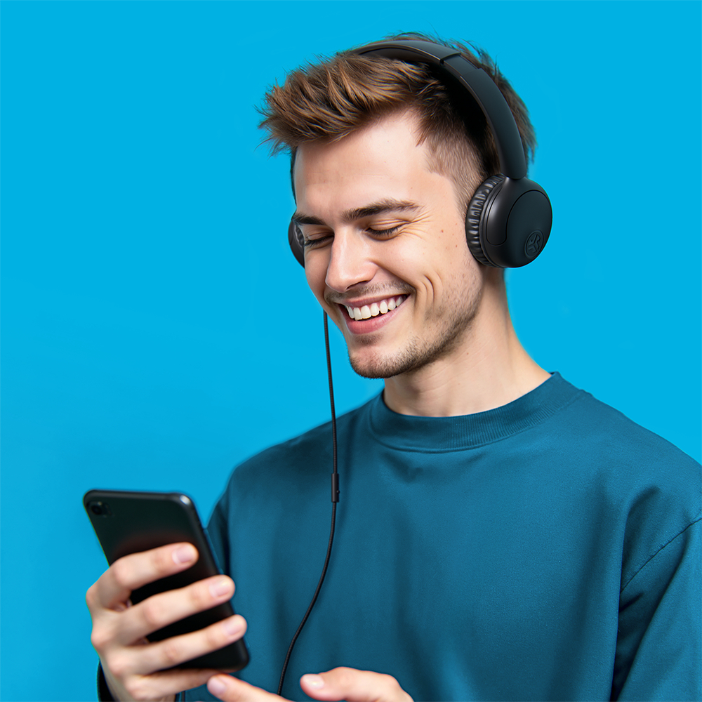 Ein lächelnder Mann mit Kopfhörern, der ein Telefon hält. Er steht vor blauem Hintergrund. Der Mann trägt ein blaues Hemd.