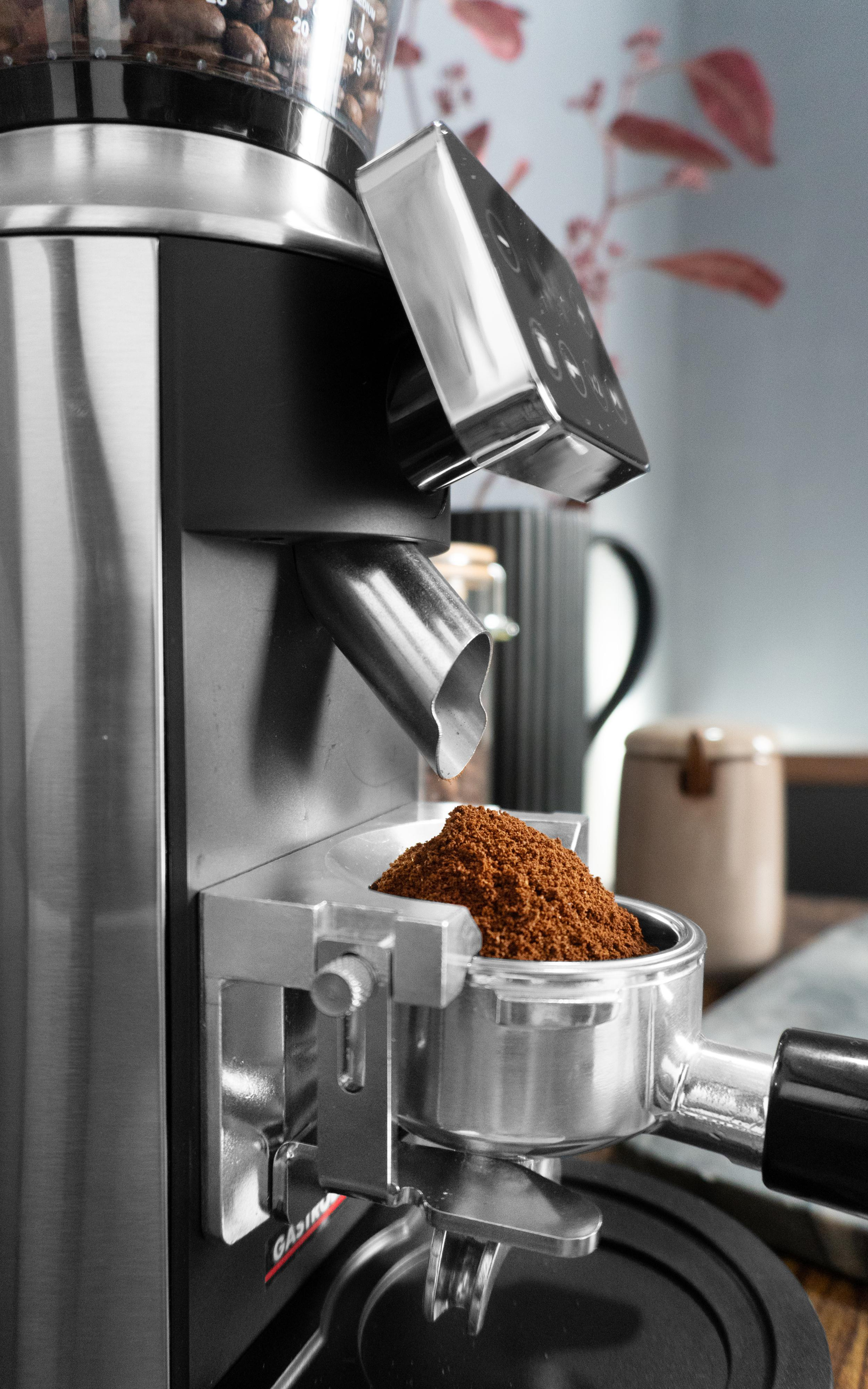 Kaffeemühle mit Kaffeepulver in einem Siebträger. Kaffeebohnen im Trichter. Edelstahl und Schwarz.