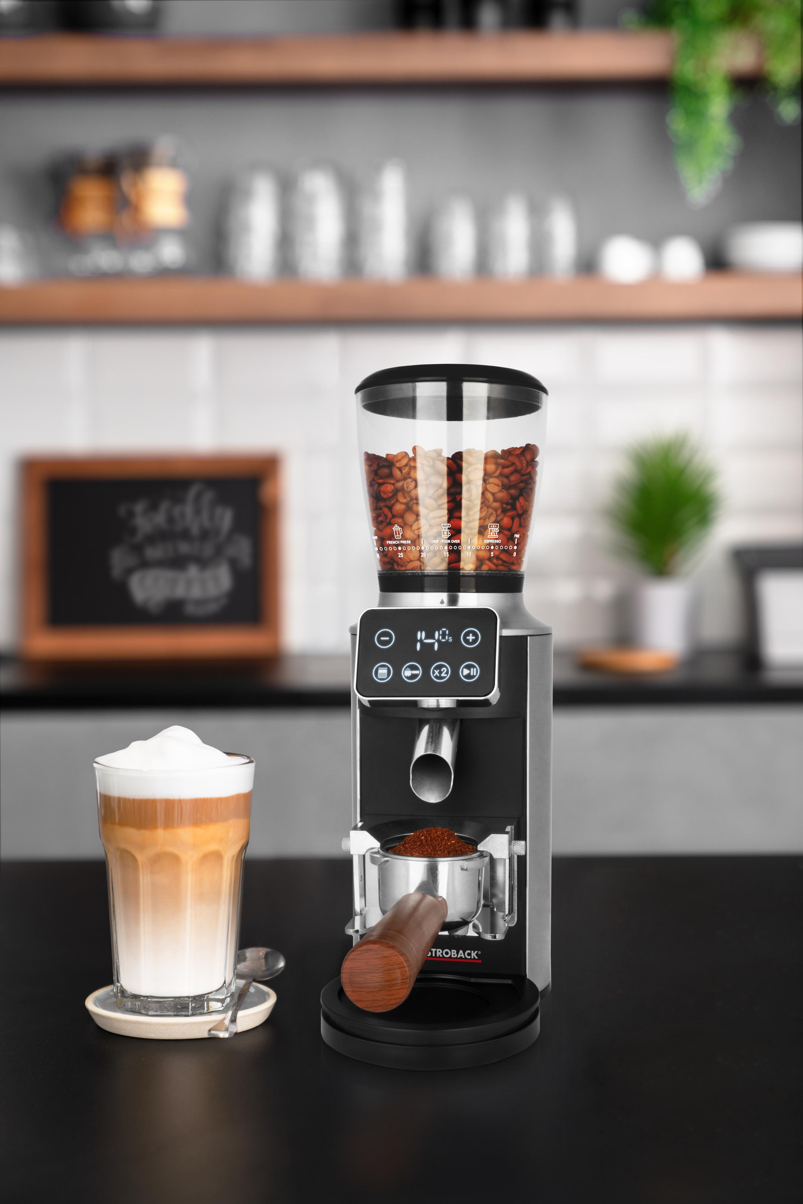 Kaffeemühle mit Bohnen, ein Latte Macchiato und eine Tafel in einer Küchenumgebung. Fokus auf Mühle und Latte.