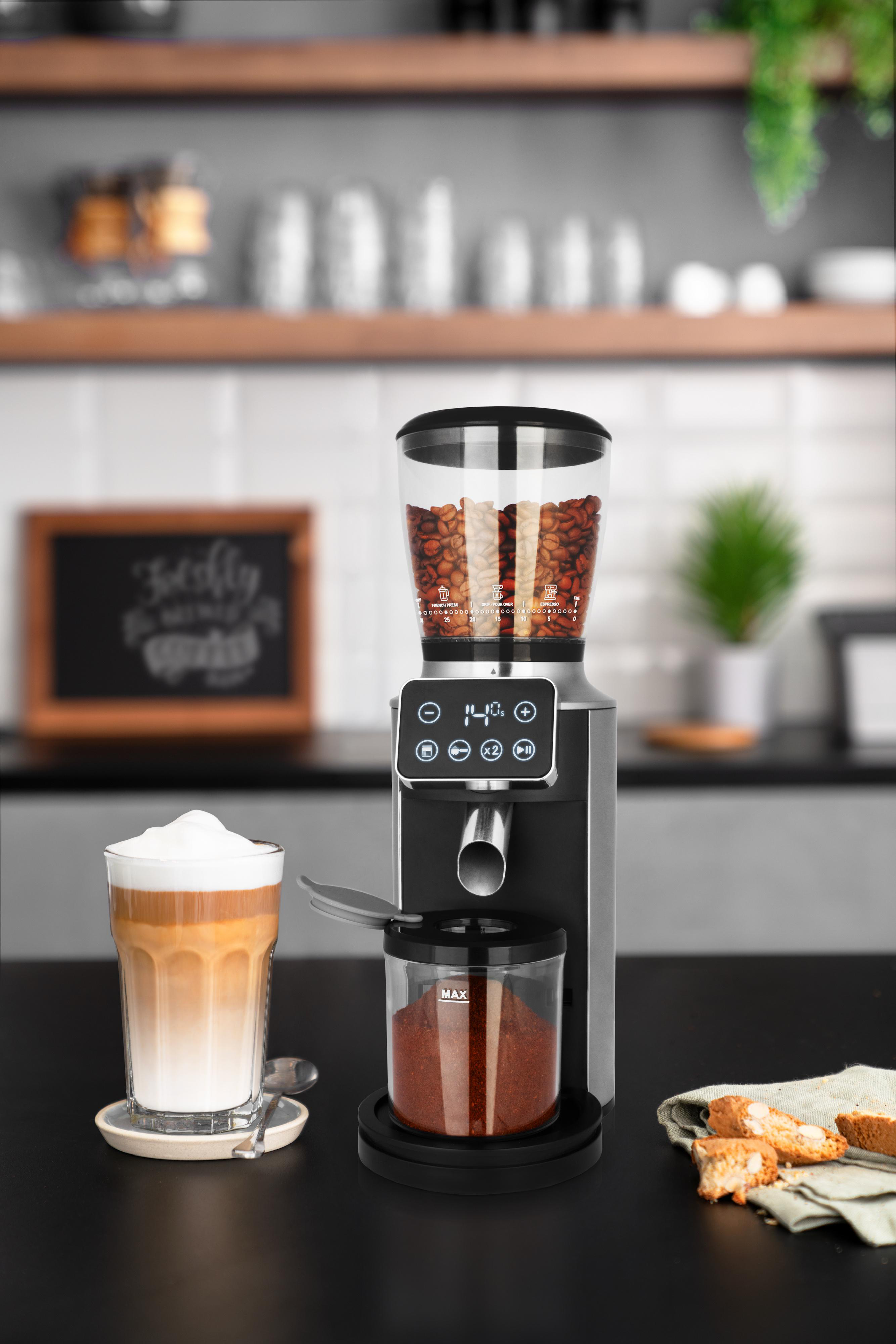 Kaffeemühle mit Bohnen, gemahlenem Kaffee, Latte und Biscotti auf einer schwarzen Theke. Im Hintergrund eine Tafel.