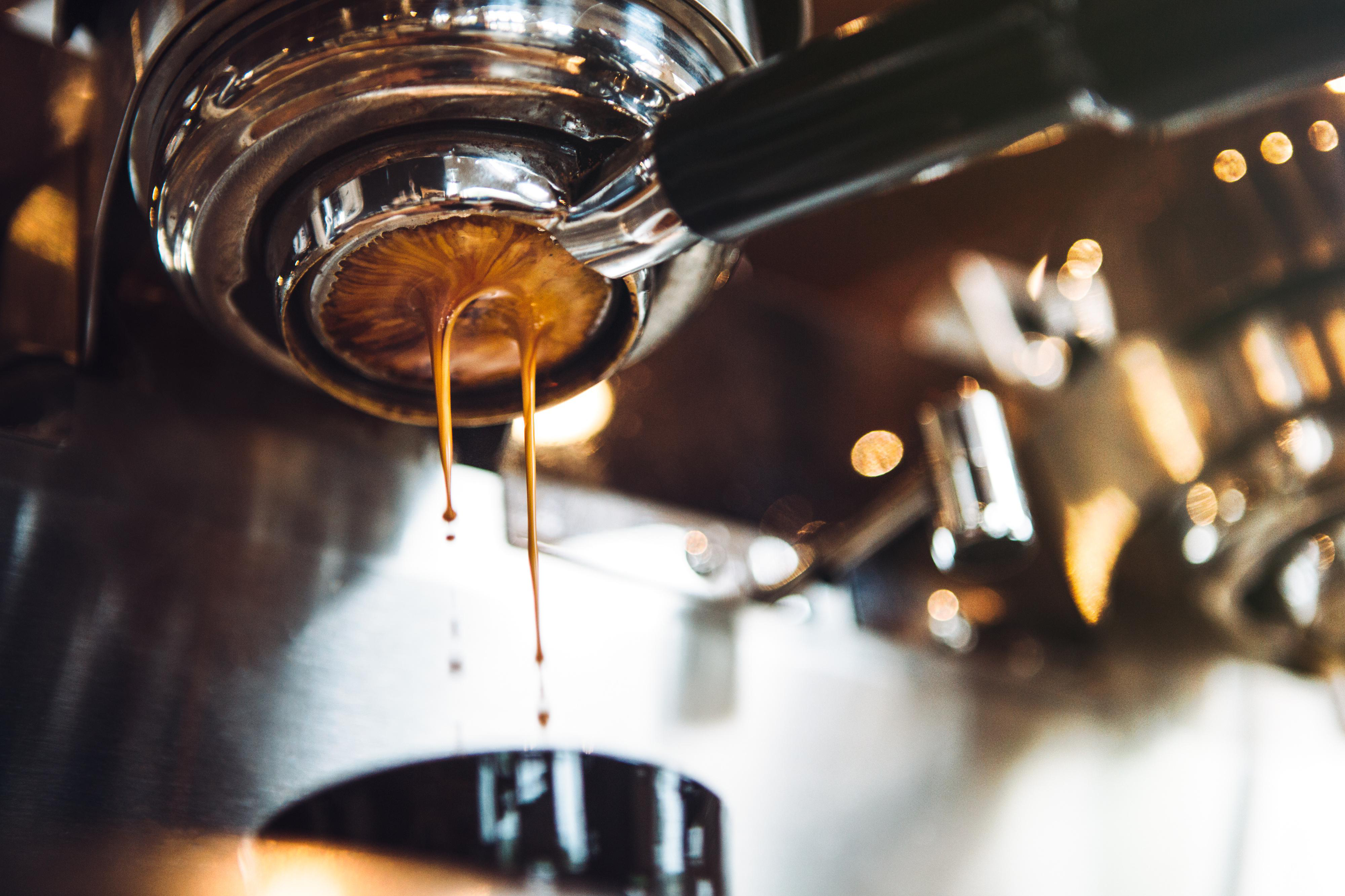 Nahaufnahme einer Espressomaschine, die Kaffee ausgibt. Dunkelbrauner Kaffee tropft aus dem Siebträger.