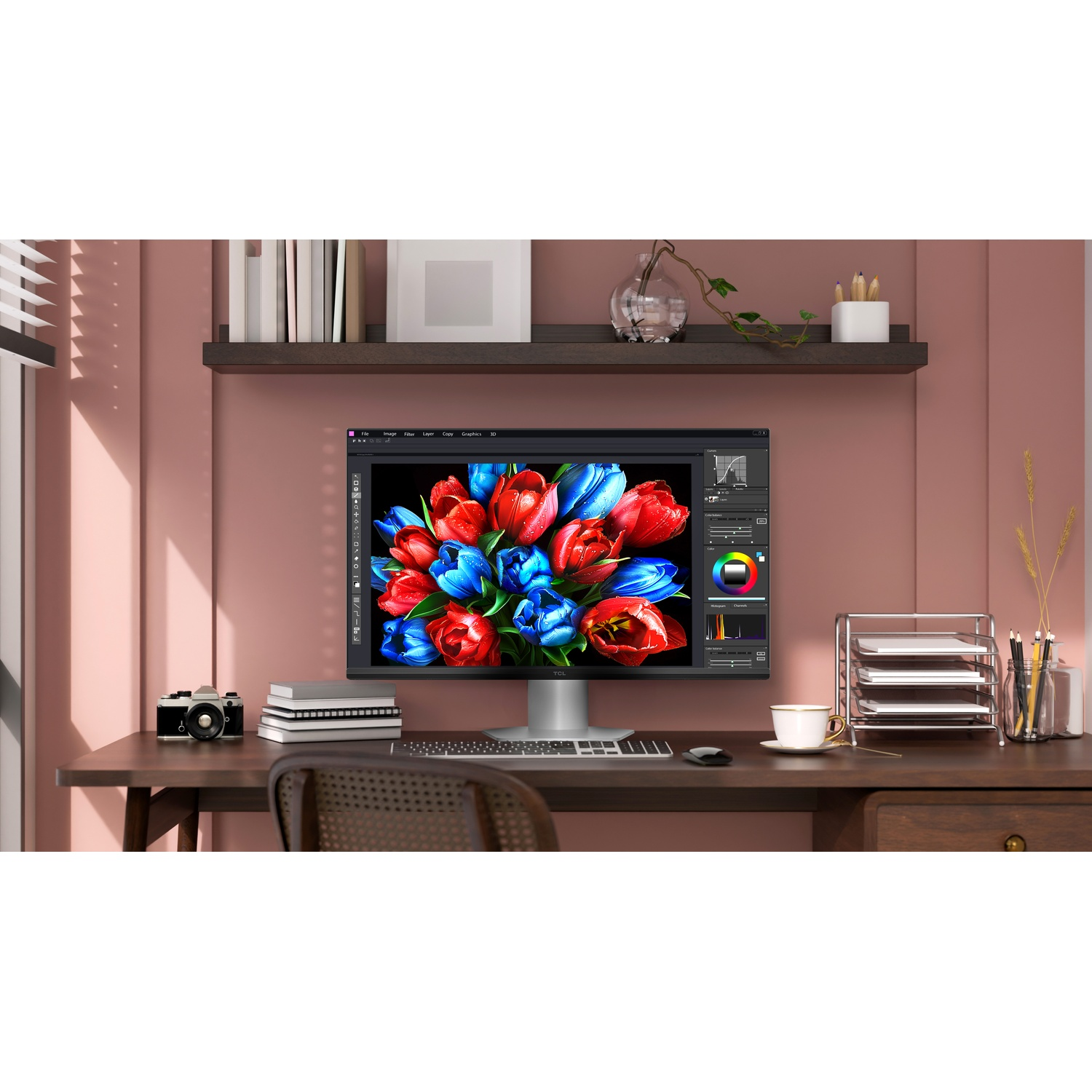 Een bureau met een computer met bloemen. Een camera, boeken en een kopje koffie staan op het bureau. Een plank met spullen erboven.