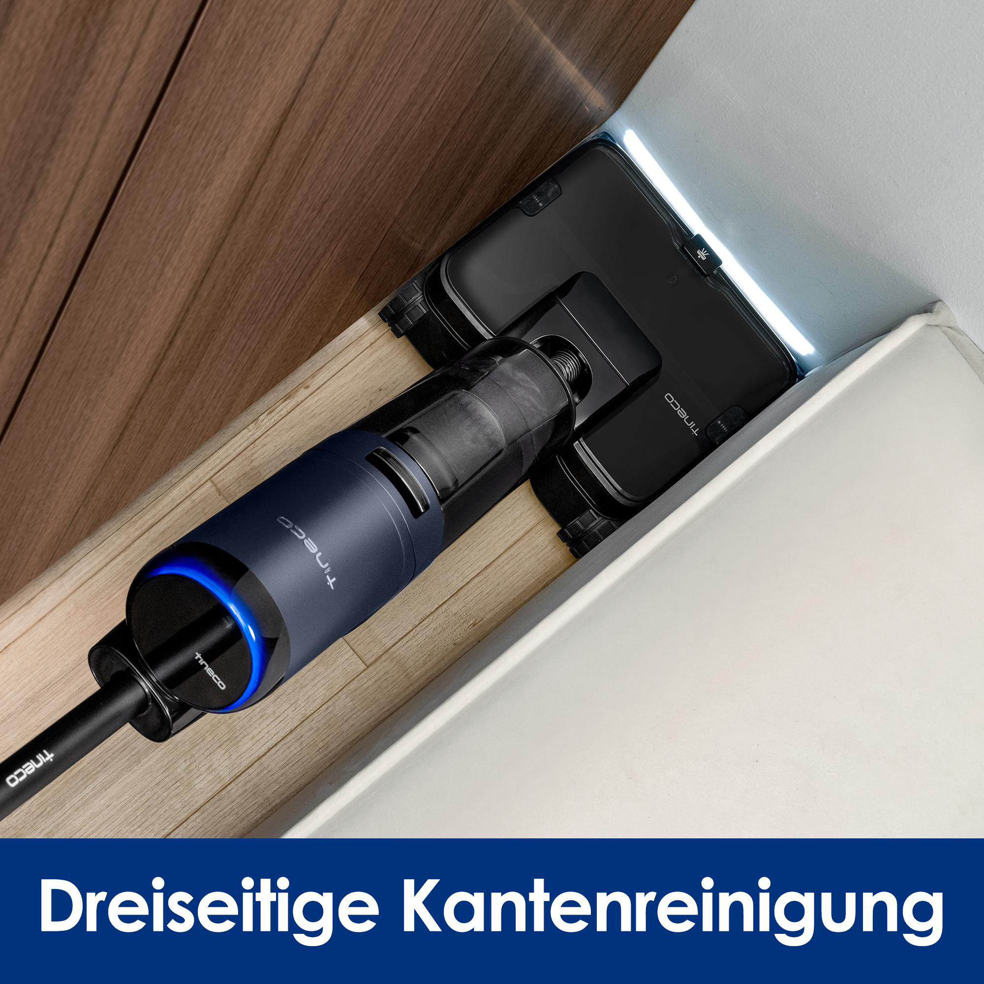 Ein dunkelblauer Staubsauger reinigt die Ecke eines Holzbodens. Der Staubsauger hat ein blaues Leuchten.