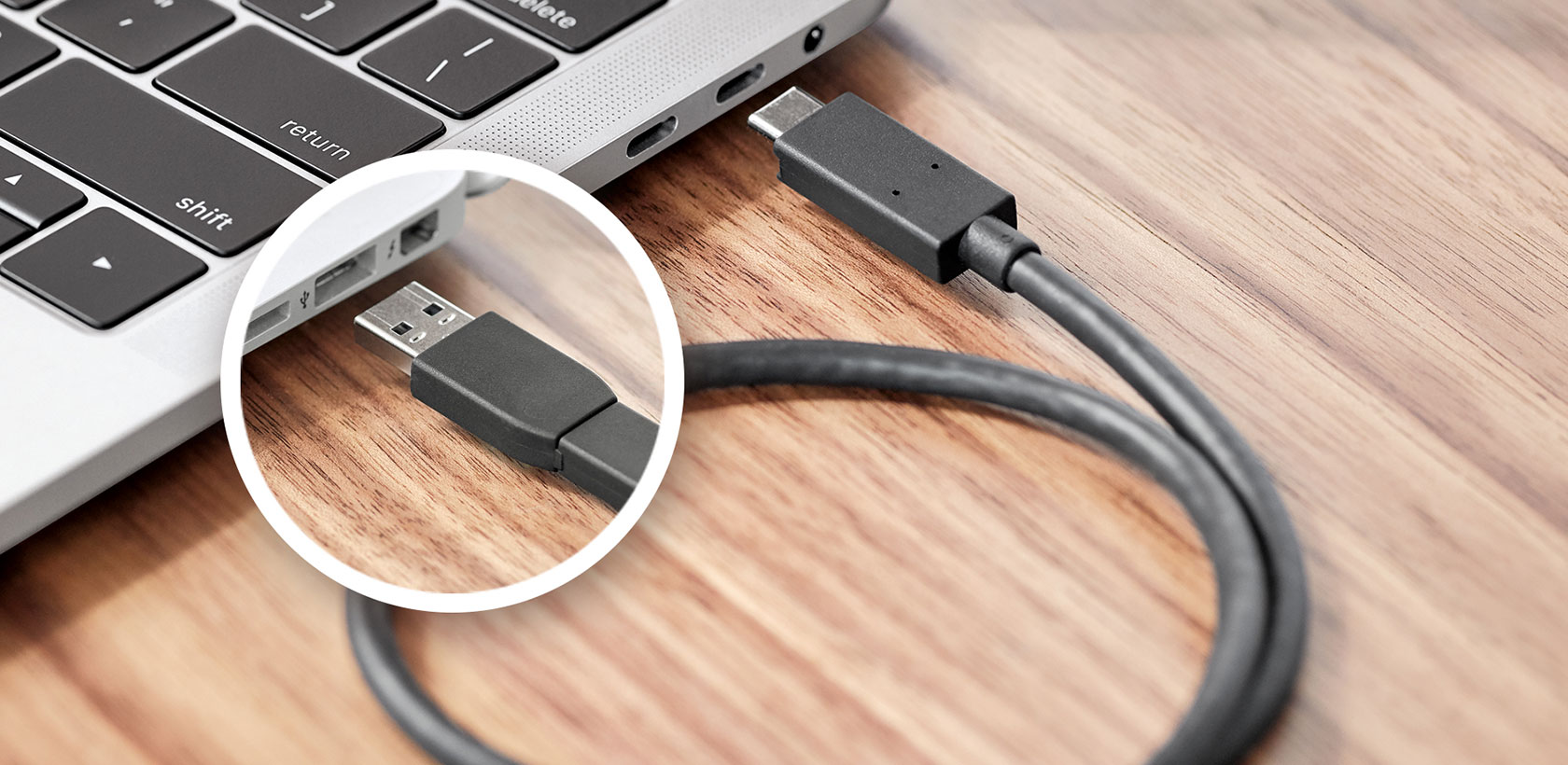 Ordinateur portable avec câbles USB-C et USB connectés. Le câble USB est branché, l'ordinateur est sur du bois.