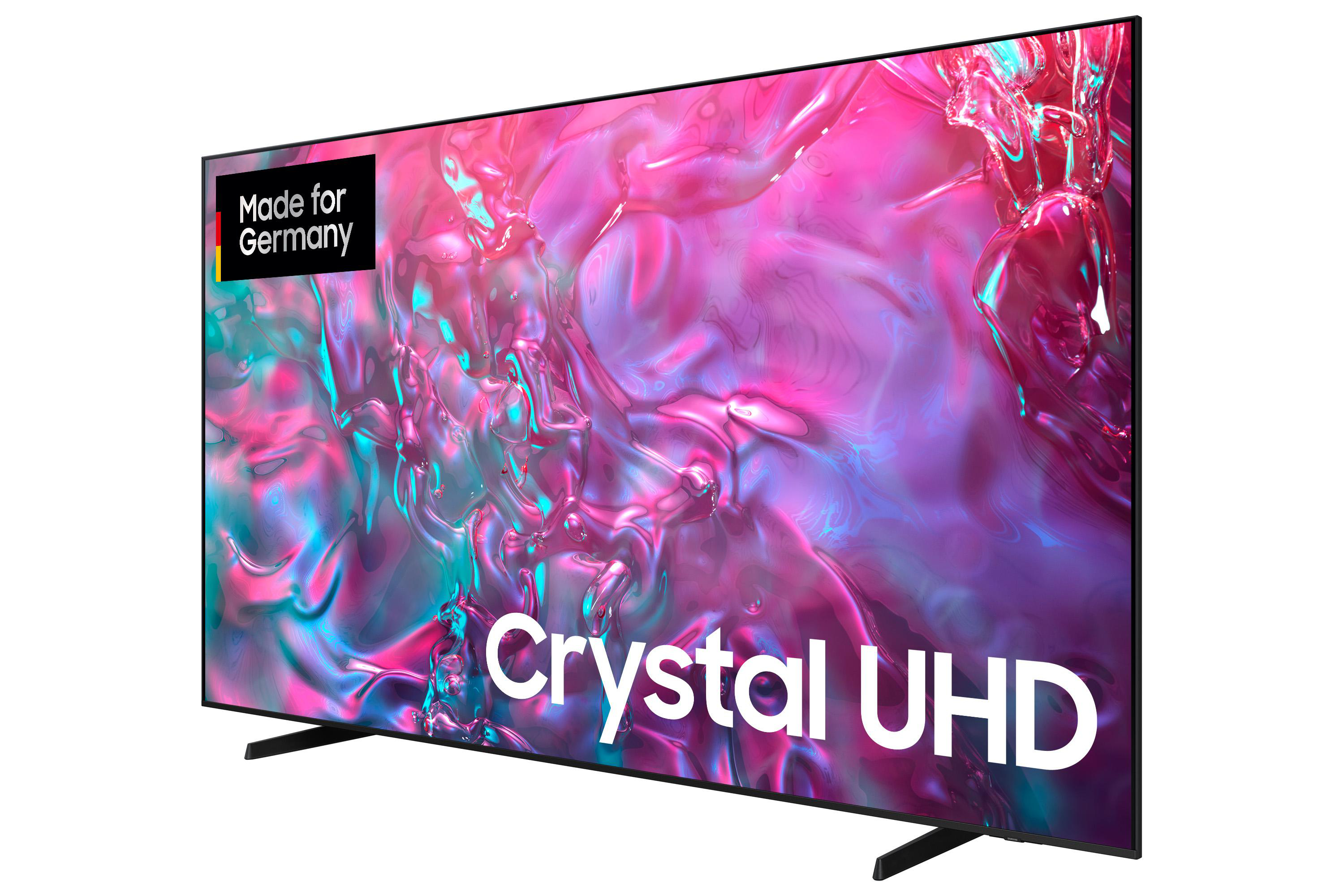 Ein Samsung Crystal UHD-Fernseher. Er hat einen schwarzen Rahmen, Ständer und einen bunten abstrakten Hintergrund. Der Fernseher ist mit 'Made for Germany' gekennzeichnet.
