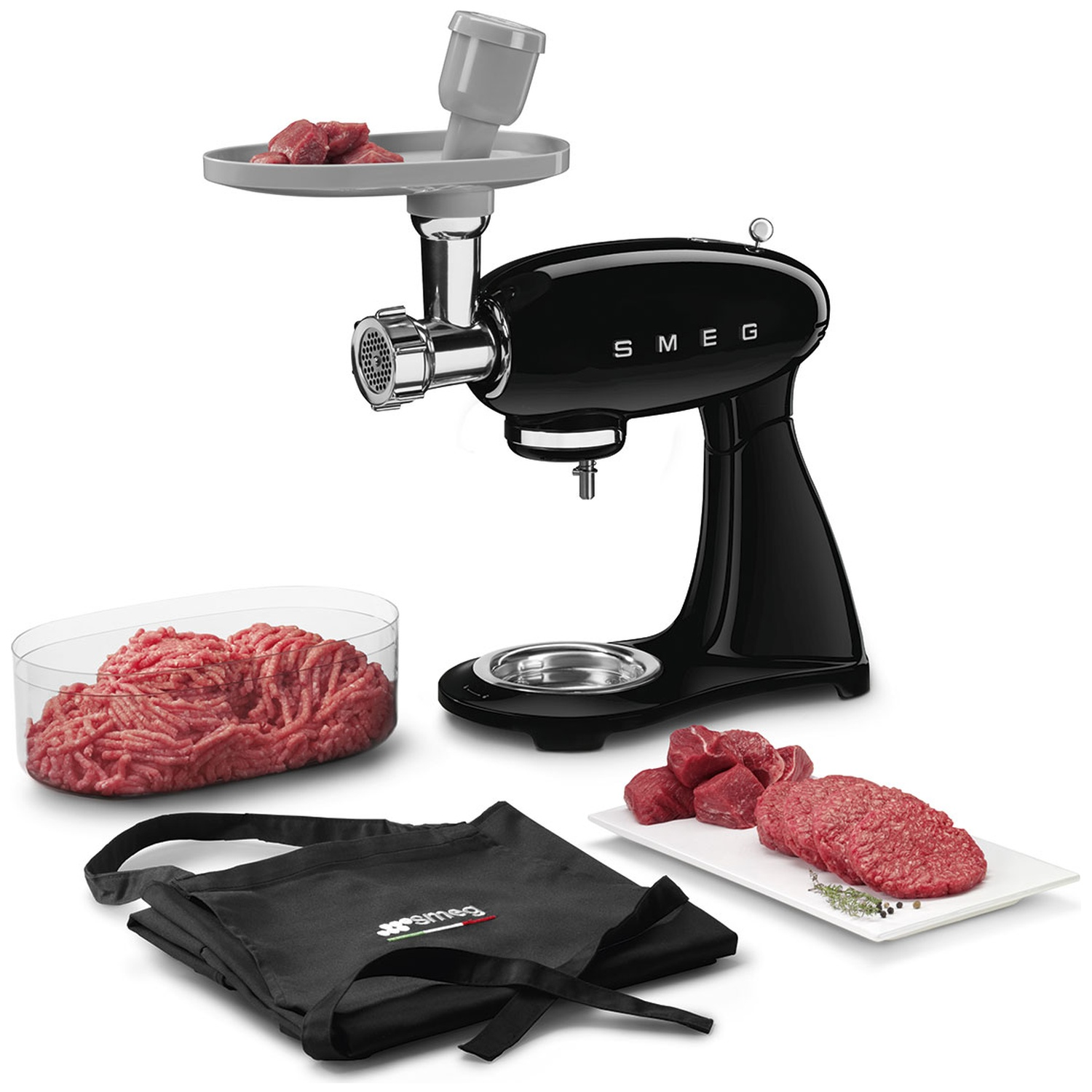 A black SMEG meat grinder with accessories, including raw meat, a container of ground meat, and an apron.
