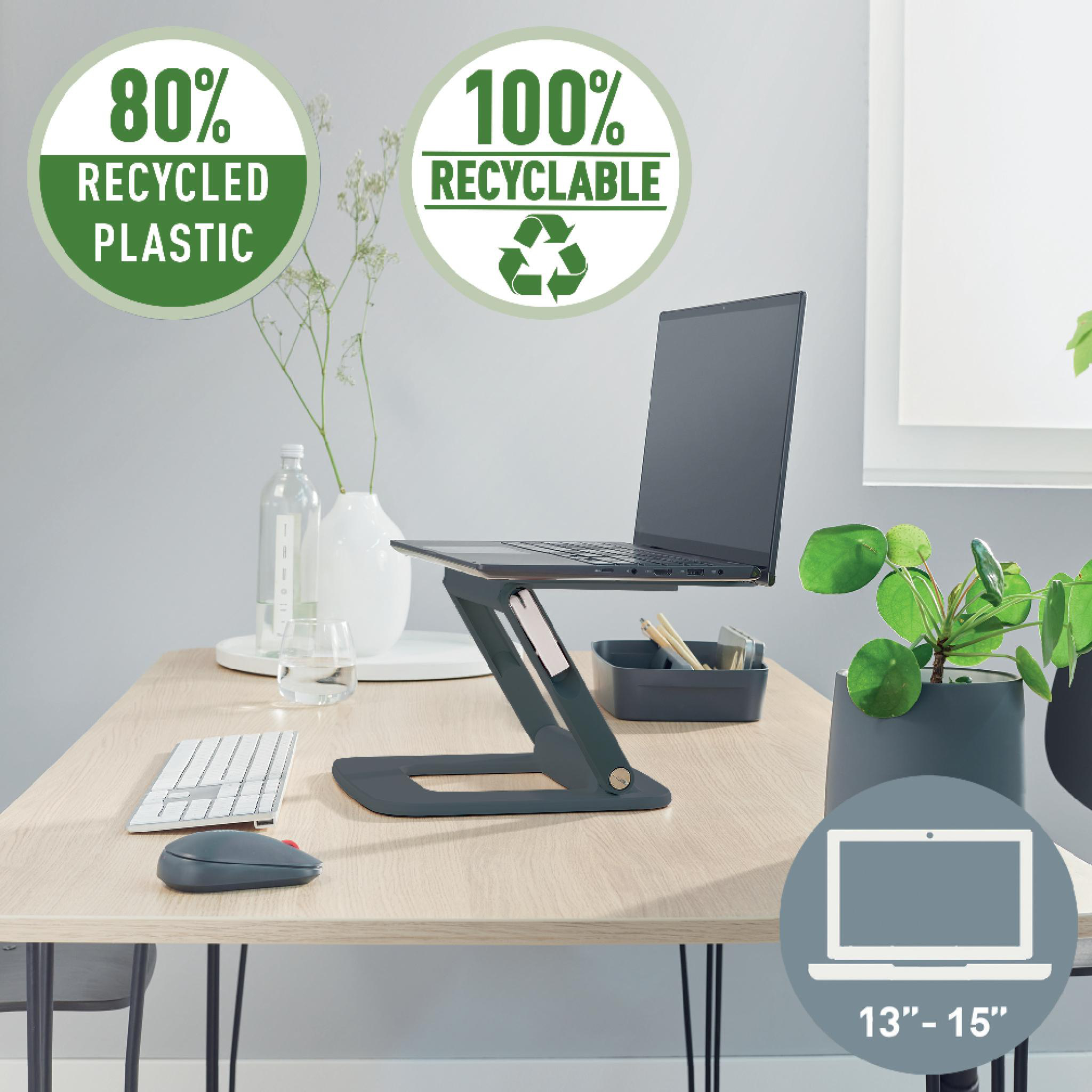 Laptop auf einem Ständer auf einem Holztisch. Enthält eine Tastatur, Maus, Pflanzen und Recycling-Etiketten.