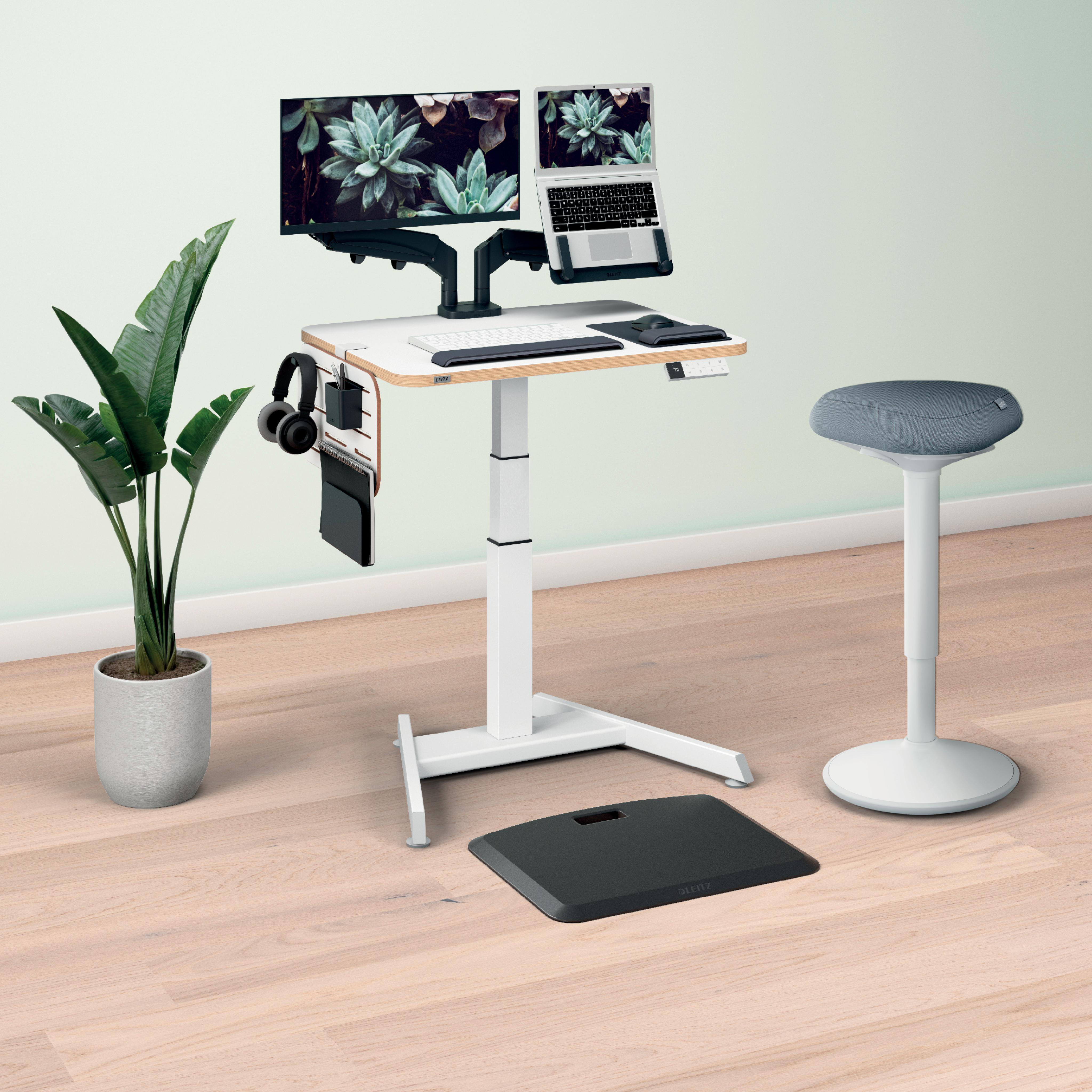 Moderne Büroeinrichtung mit Stehpult, Monitor, Laptop, Hocker, Pflanze und Zubehör auf Holzboden.