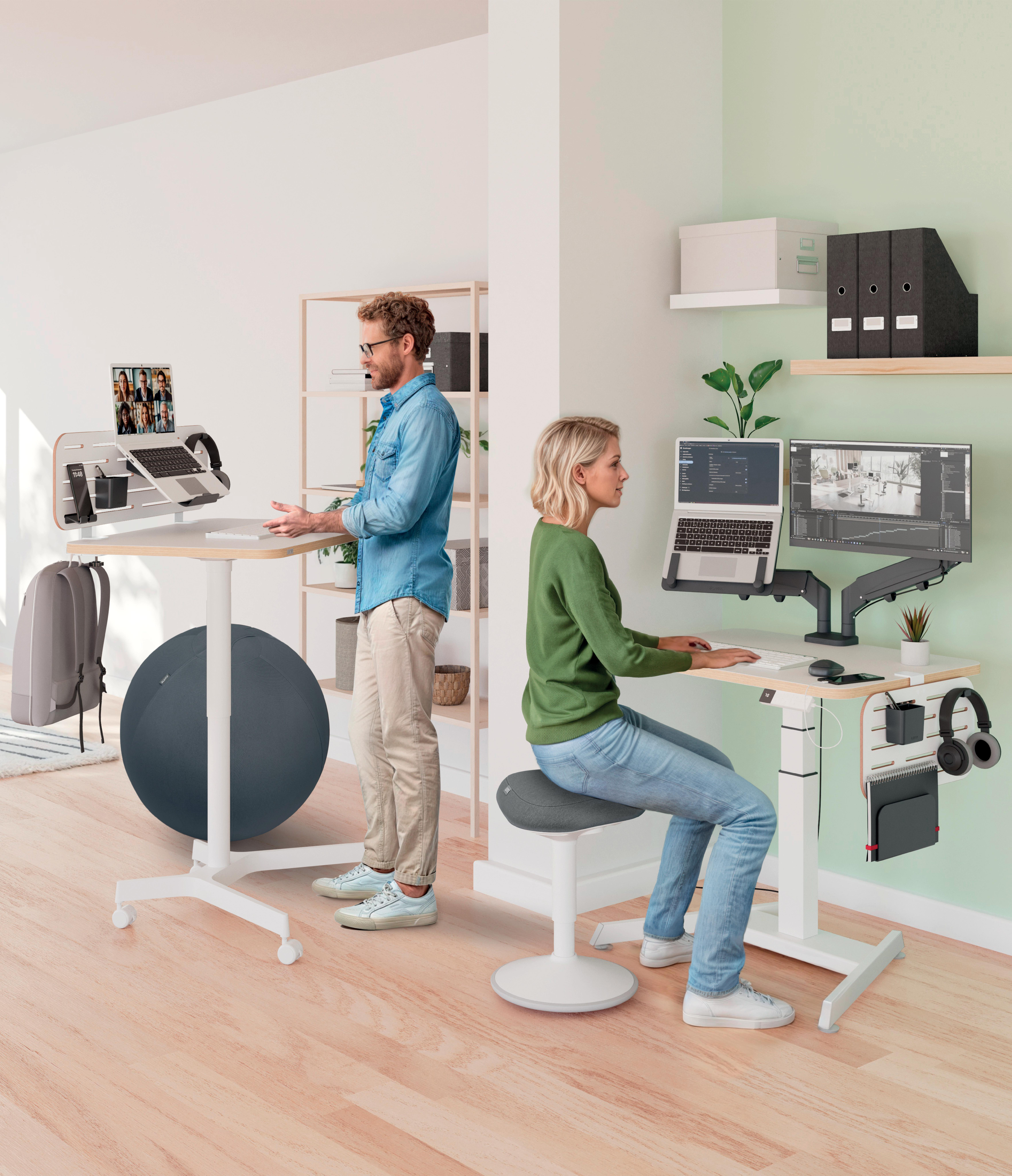 Zwei Personen an Schreibtischen. Ein Mann steht an einem Laptop, die andere sitzt an einem Schreibtisch mit Monitor.