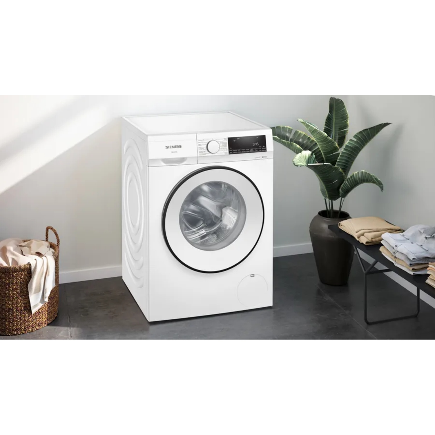 Un lave-linge blanc dans une pièce. Panier de linge à gauche, banc avec vêtements pliés à droite.