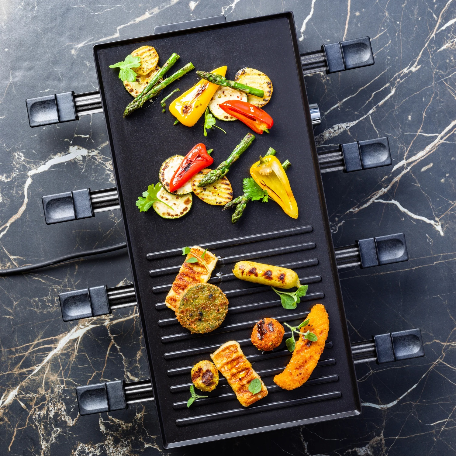 Gegrilde groenten en andere etenswaren op een zwarte grill, tegen een marmeren achtergrond. Inclusief paprika's, asperges en andere items.