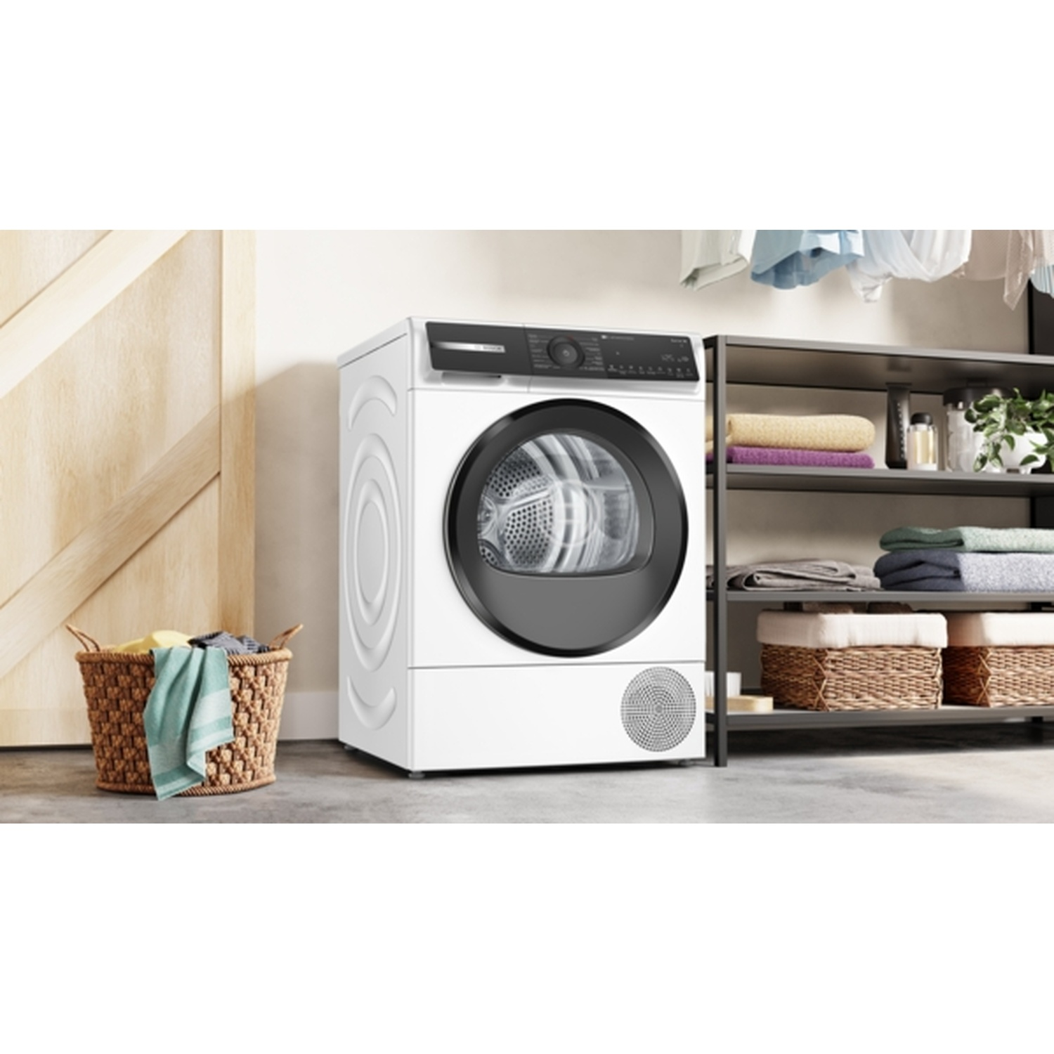Un sèche-linge blanc se trouve à côté d'une porte en bois et d'une étagère métallique avec des serviettes pliées et des paniers. Un panier à linge à gauche.