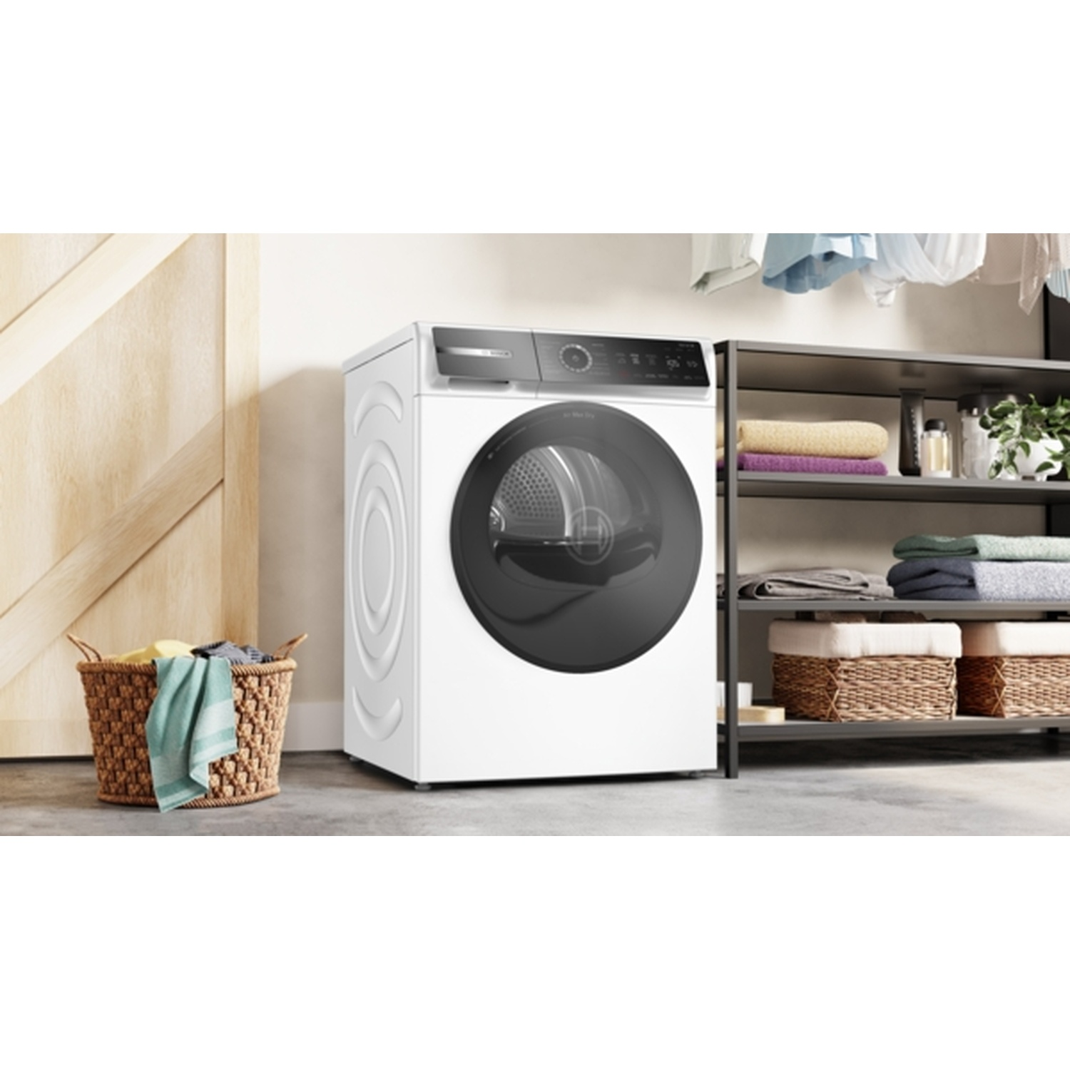 A white washing machine stands next to a wooden door. A basket with clothes sits on the floor. Shelves with towels are on the right.