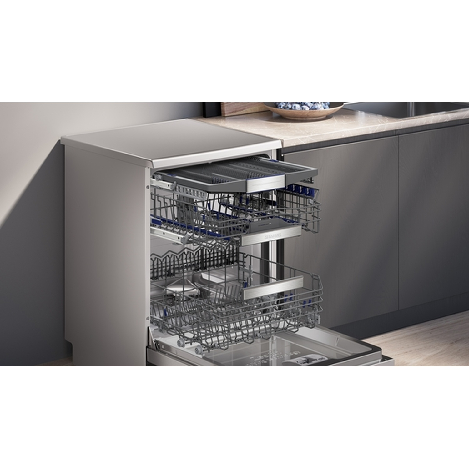 Lave-vaisselle ouvert avec deux paniers. Ustensiles visibles à l'intérieur. La machine est grise, placée à côté d'un meuble gris foncé.