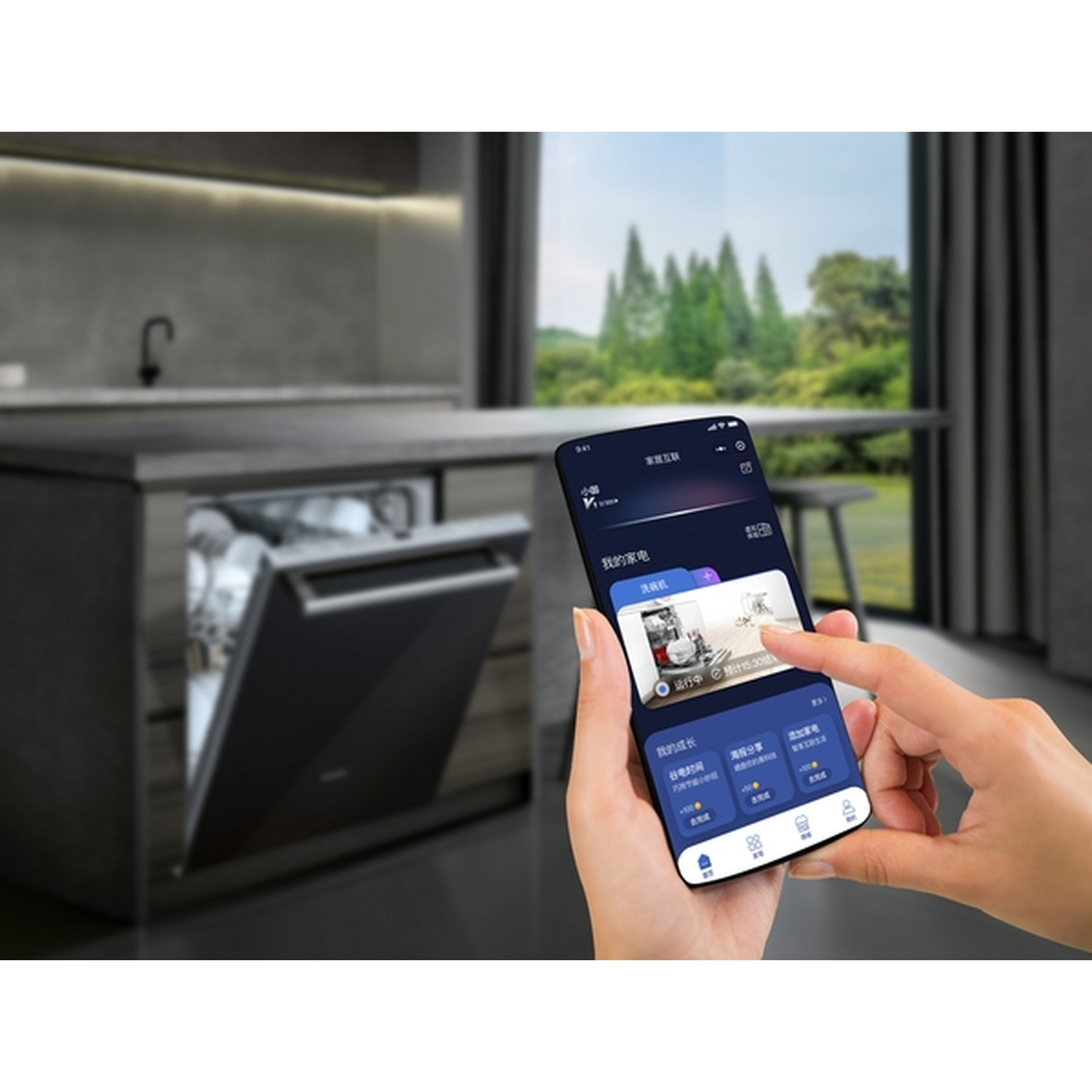 Une main tenant un smartphone affichant une application de lave-vaisselle, avec un lave-vaisselle ouvert en arrière-plan. Des arbres verts sont visibles à travers une fenêtre.