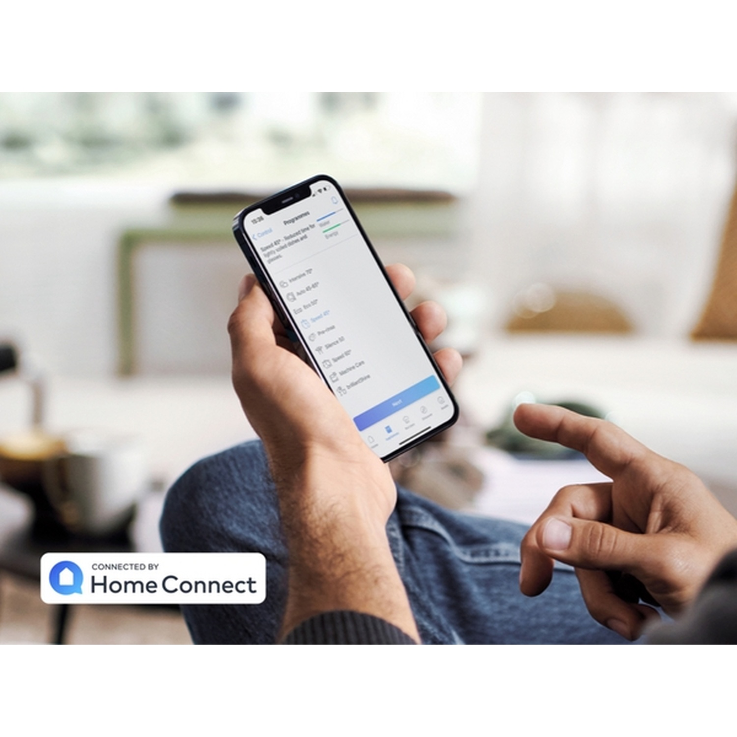 Une personne tient un smartphone affichant une interface d'application. L'écran montre des options de programme. Le logo Home Connect est visible.