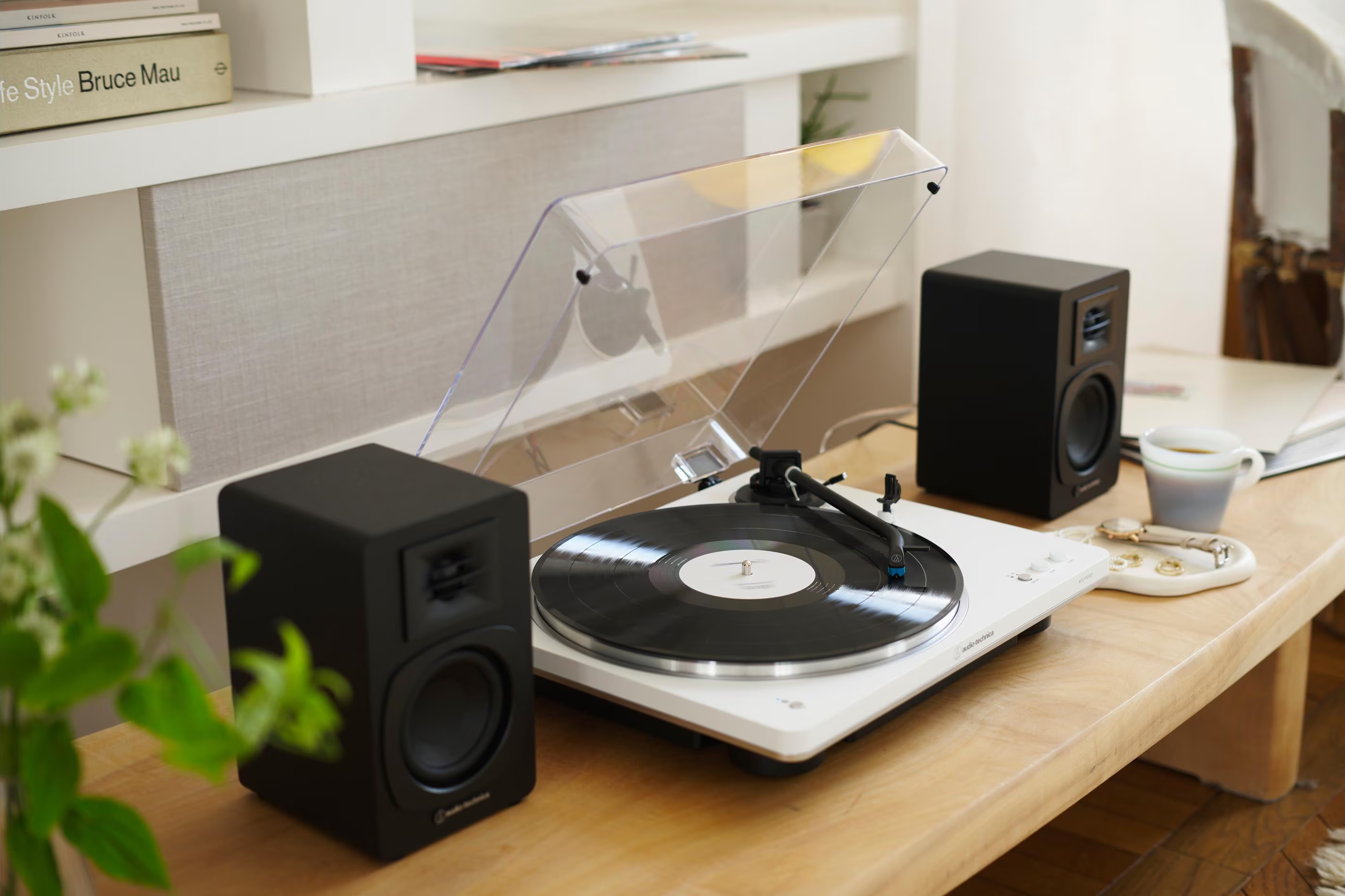 Un giradischi con un disco in vinile nero è su un tavolo di legno. Ci sono altoparlanti neri su entrambi i lati.