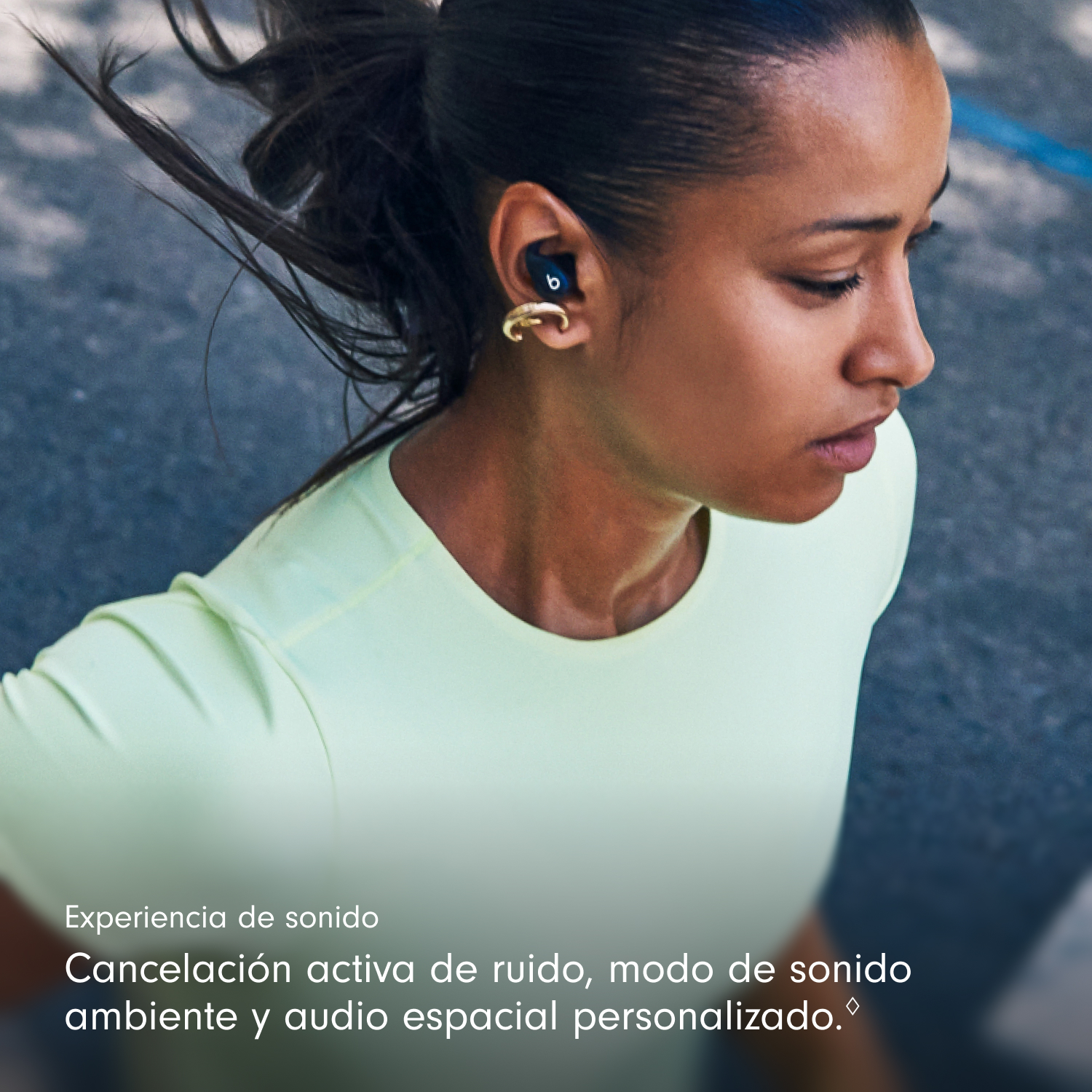 Una mujer con auriculares corre. Tiene cabello oscuro y viste una camisa verde claro. Tiene un pendiente dorado.