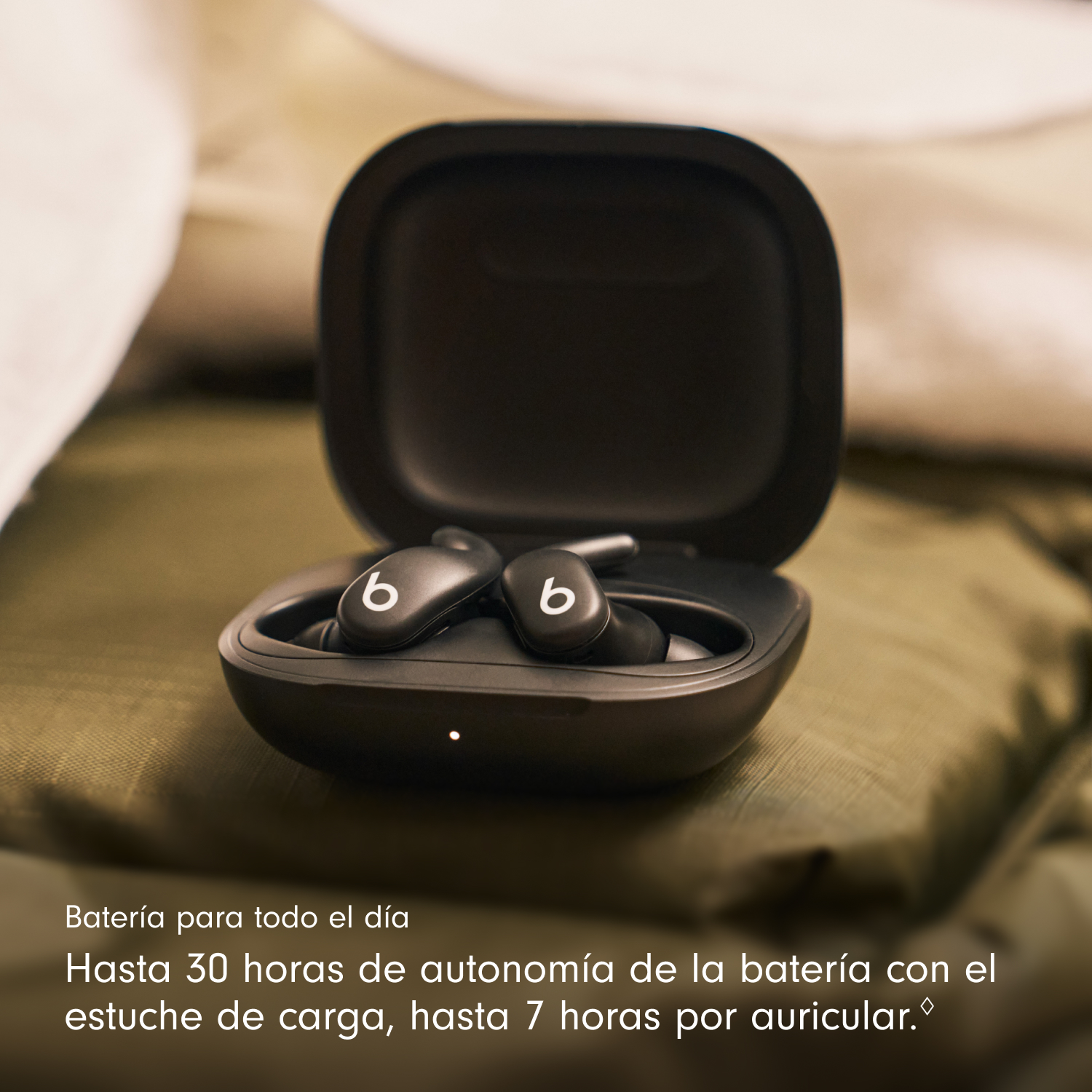 Auriculares Beats negros en un estuche abierto sobre una superficie verde. Logotipo 'b' blanco en cada auricular. Texto debajo.