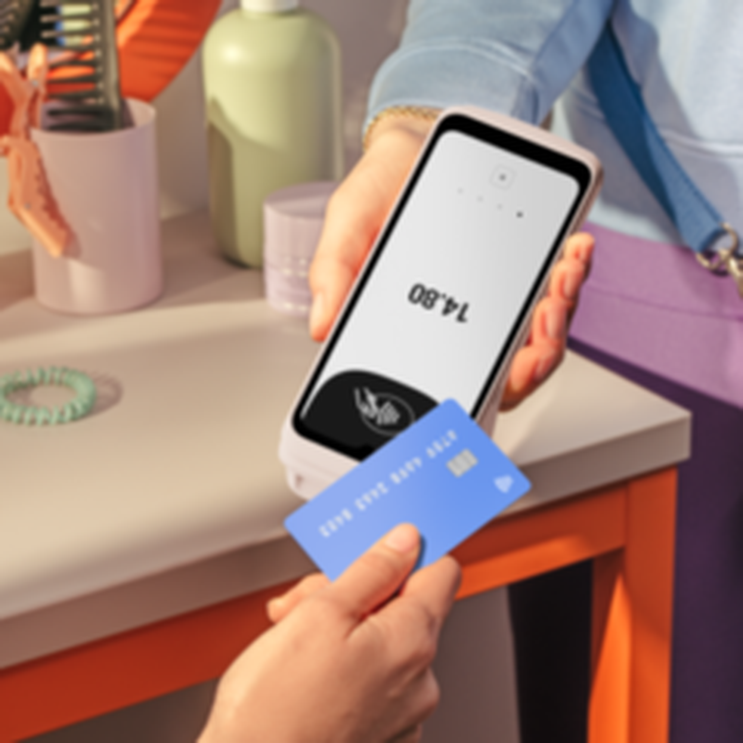 Une personne paie avec une carte de crédit. Un appareil de point de vente affiche 14,80 $. La carte est bleue, l'appareil est tenu par une personne.