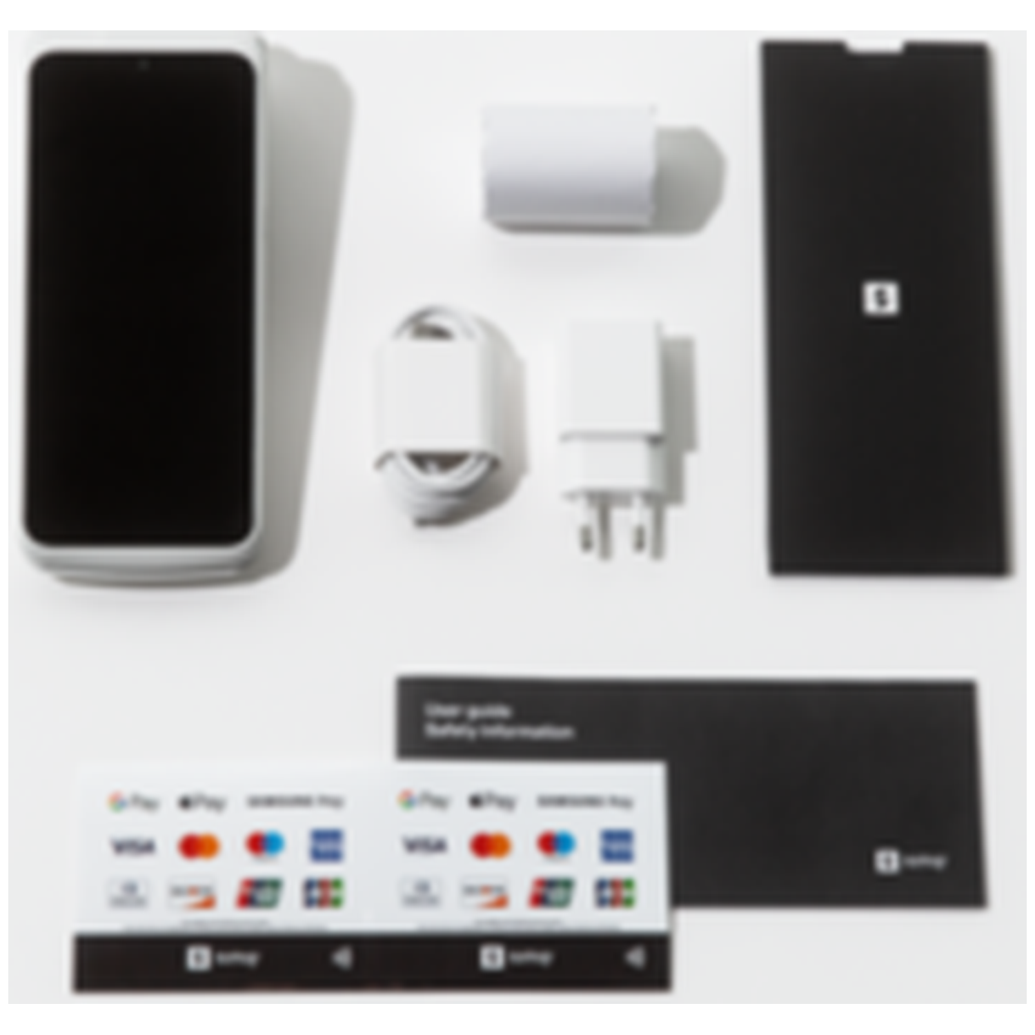 Un smartphone, un chargeur, un câble et de la documentation sont disposés sur une surface blanche. Le téléphone est blanc avec un écran noir.