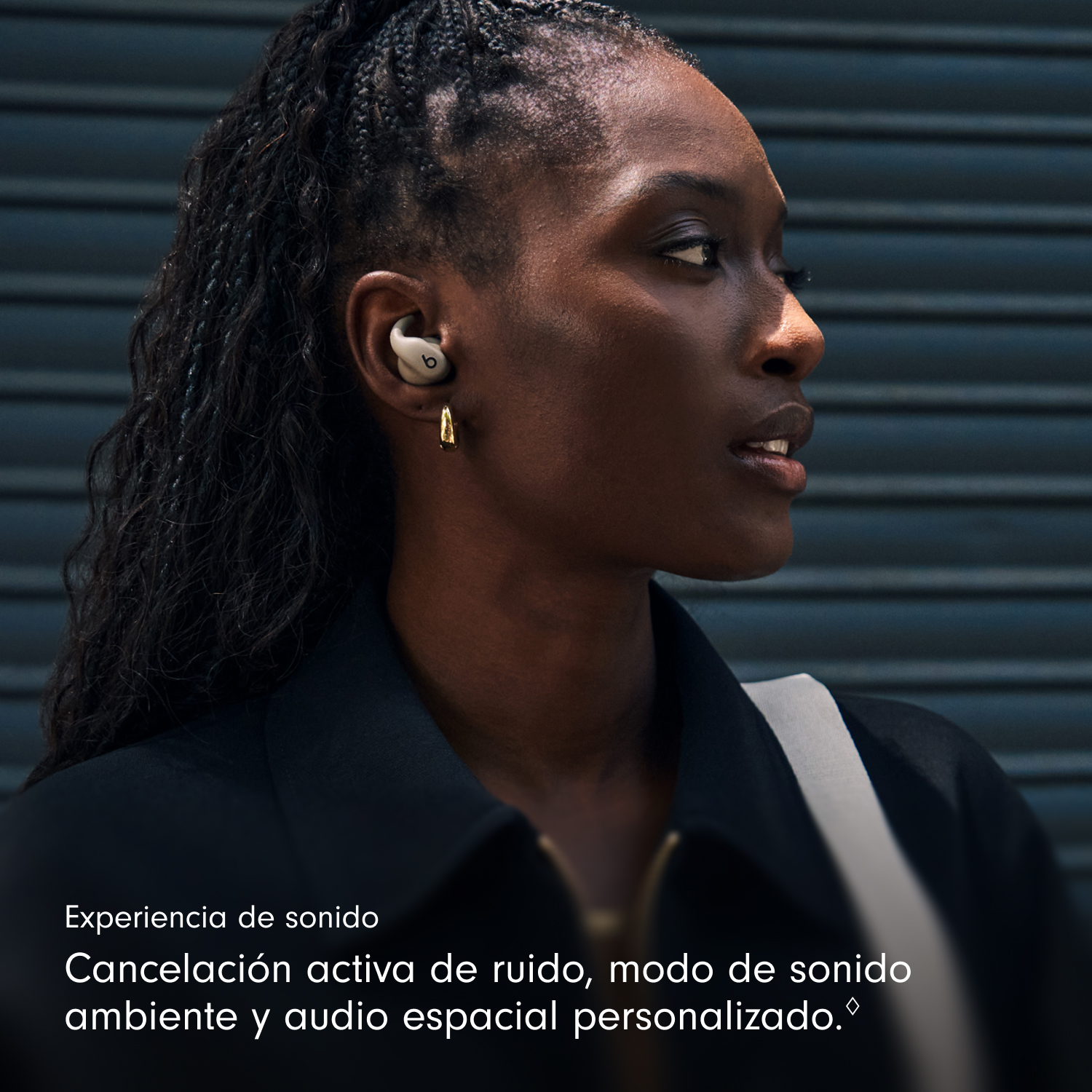 Una mujer negra con auriculares Beats mira hacia un lado. Lleva una camisa negra, tiene el pelo oscuro y un pendiente dorado.