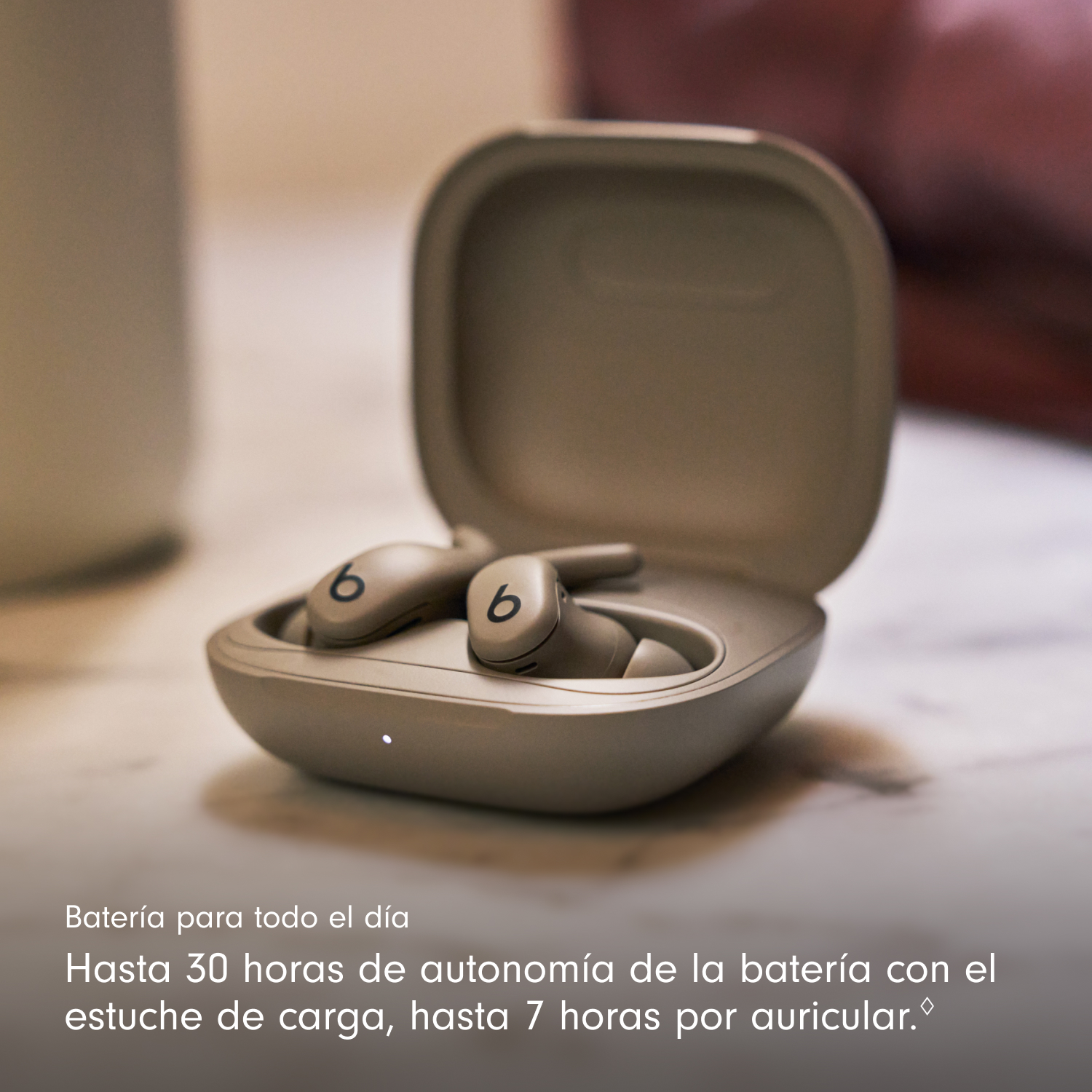 Estuche de auriculares beige abierto con dos auriculares dentro. Cada uno tiene un '6'. El texto de abajo dice: 'Batería para todo el día'.