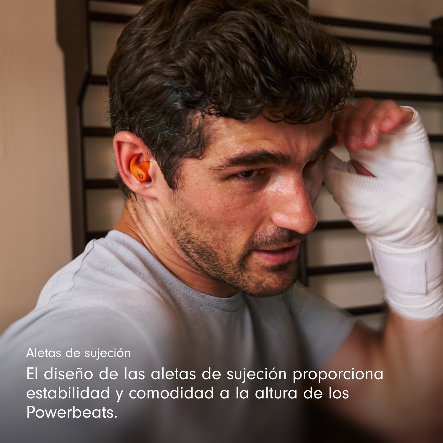 Un hombre con auriculares naranjas en la oreja, mano vendada, sudando. Texto: 'Aletas de sujeción'. El diseño proporciona estabilidad y comodidad.