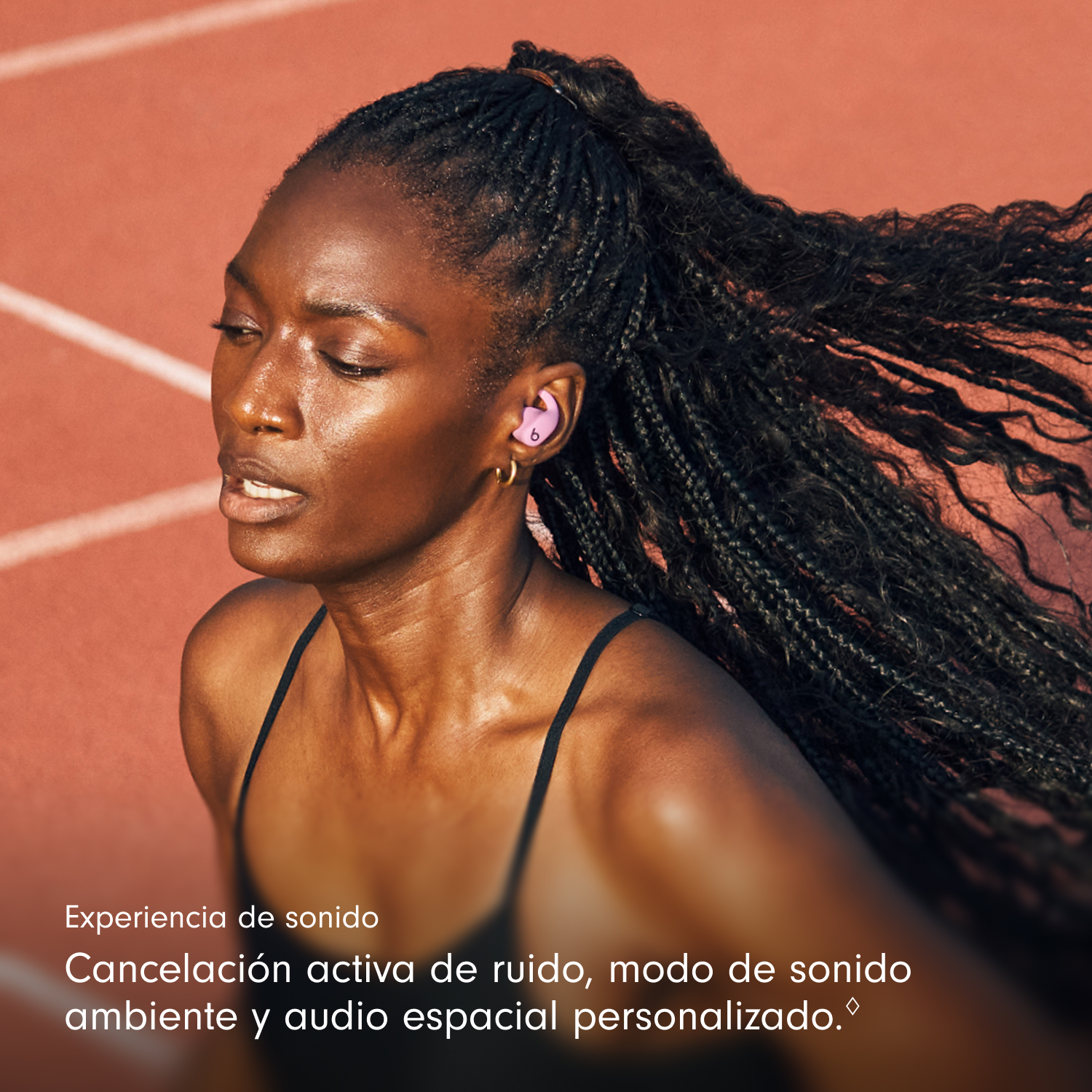 Una mujer con trenzas usa auriculares rosas, corriendo en una pista. Lleva una camiseta sin mangas negra. El fondo es una pista roja.