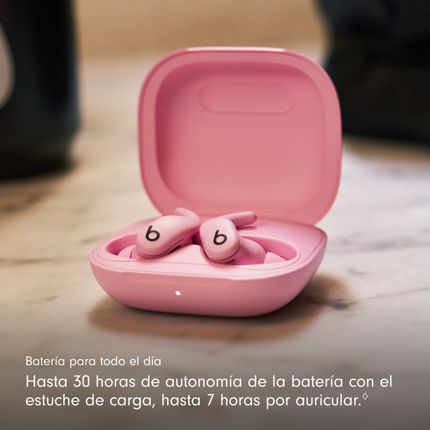 Auriculares Beats rosas en un estuche abierto. Los auriculares tienen un logotipo 'b'. El estuche está sobre una superficie de mármol, con texto abajo.