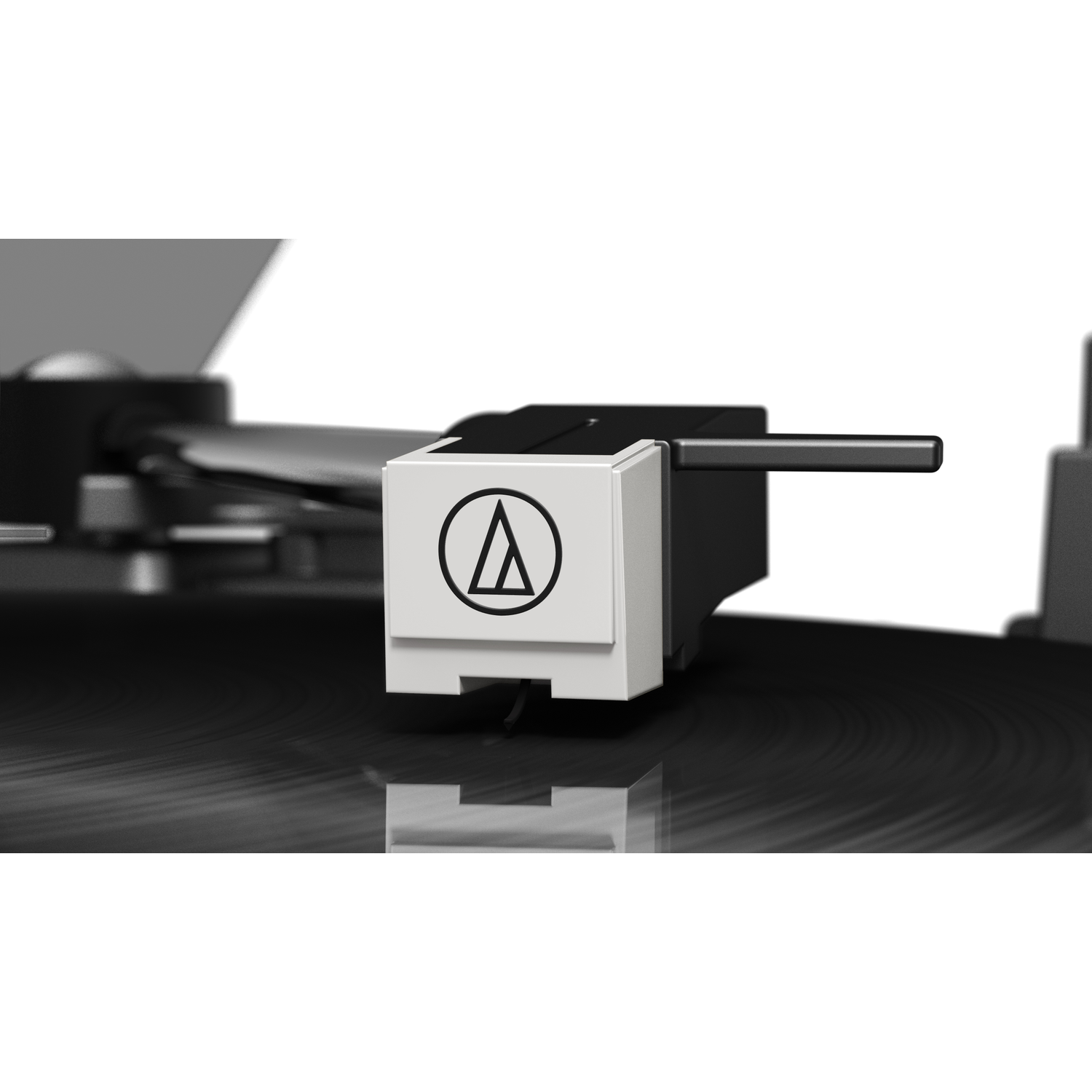 Close-up of a turntable needle. The needle is white with a black logo, resting on a black record. Background is white and blurred.
