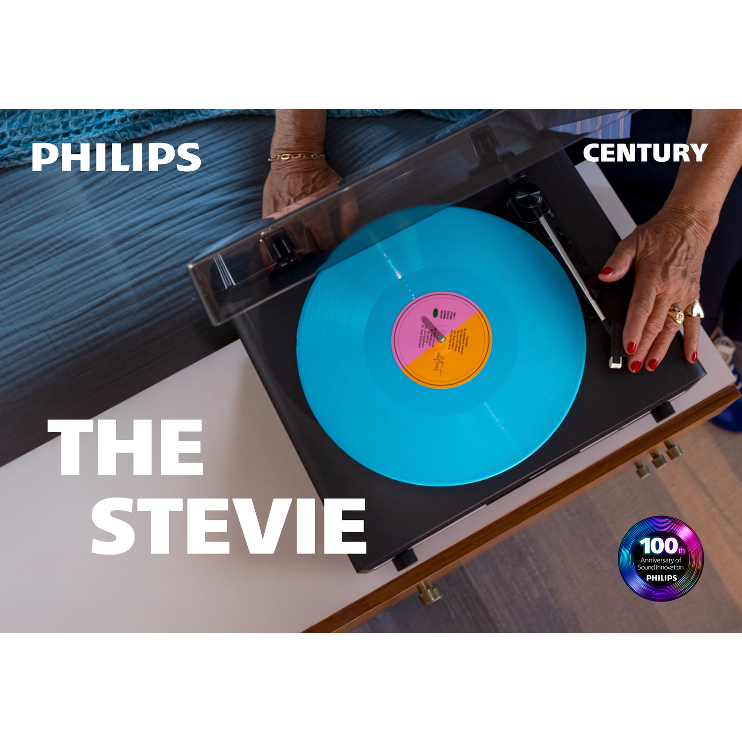 A turntable with a blue record is being handled by a person. The Philips logo is visible, along with "The Stevie" text.