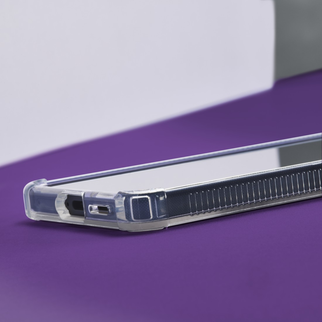 Eine transparente Handyhülle liegt auf einer violetten Oberfläche. Der Rand des Telefons ist sichtbar, mit Ladeanschluss.