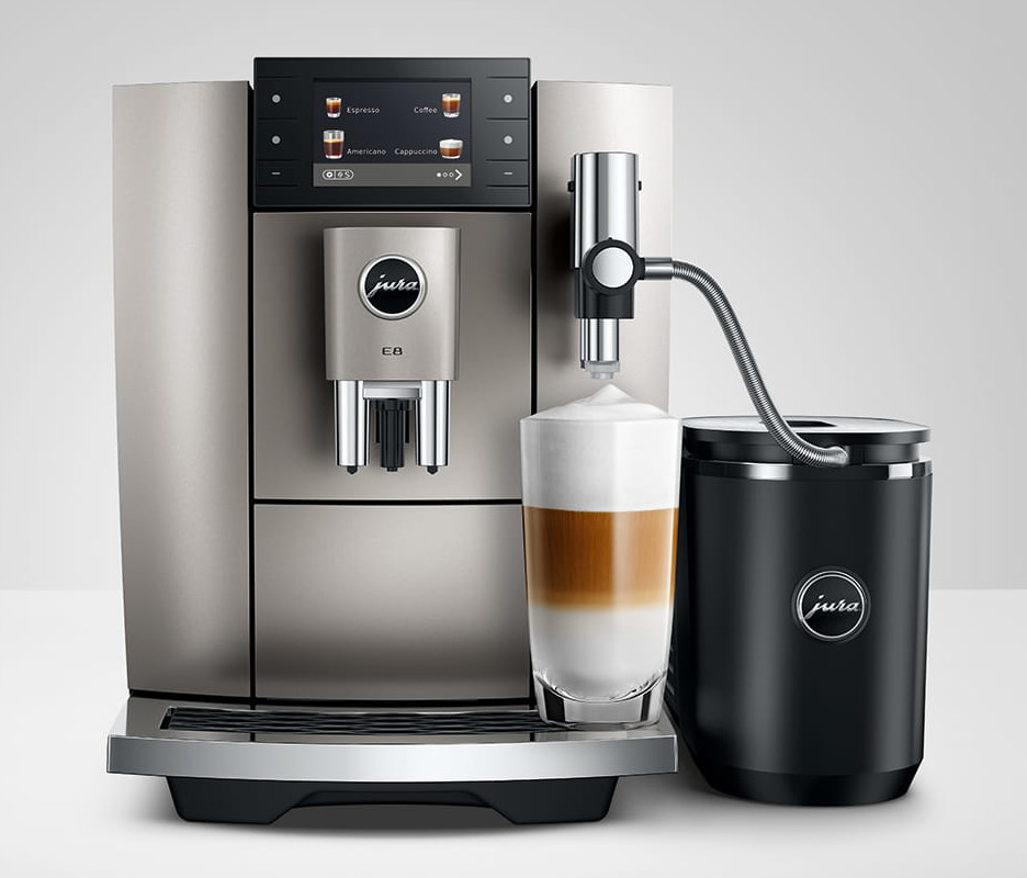 Srebrny ekspres do kawy Jura E8 ze szklanką warstwowego latte. Po prawej stronie czarny spieniacz do mleka.