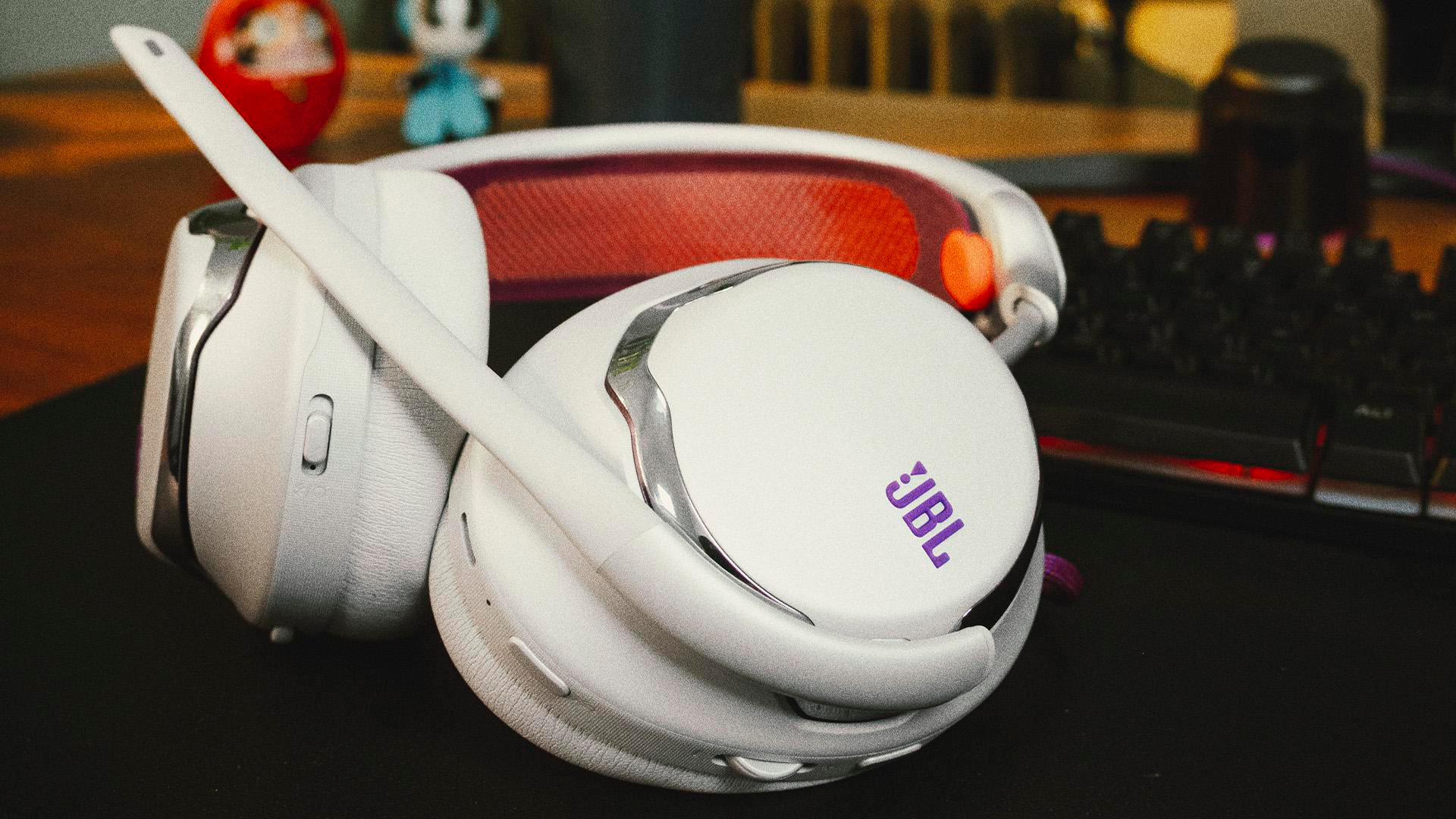 Weiße JBL-Kopfhörer auf einem Tisch. Das Logo ist sichtbar. Eine Tastatur und kleine Spielzeuge sind im Hintergrund.