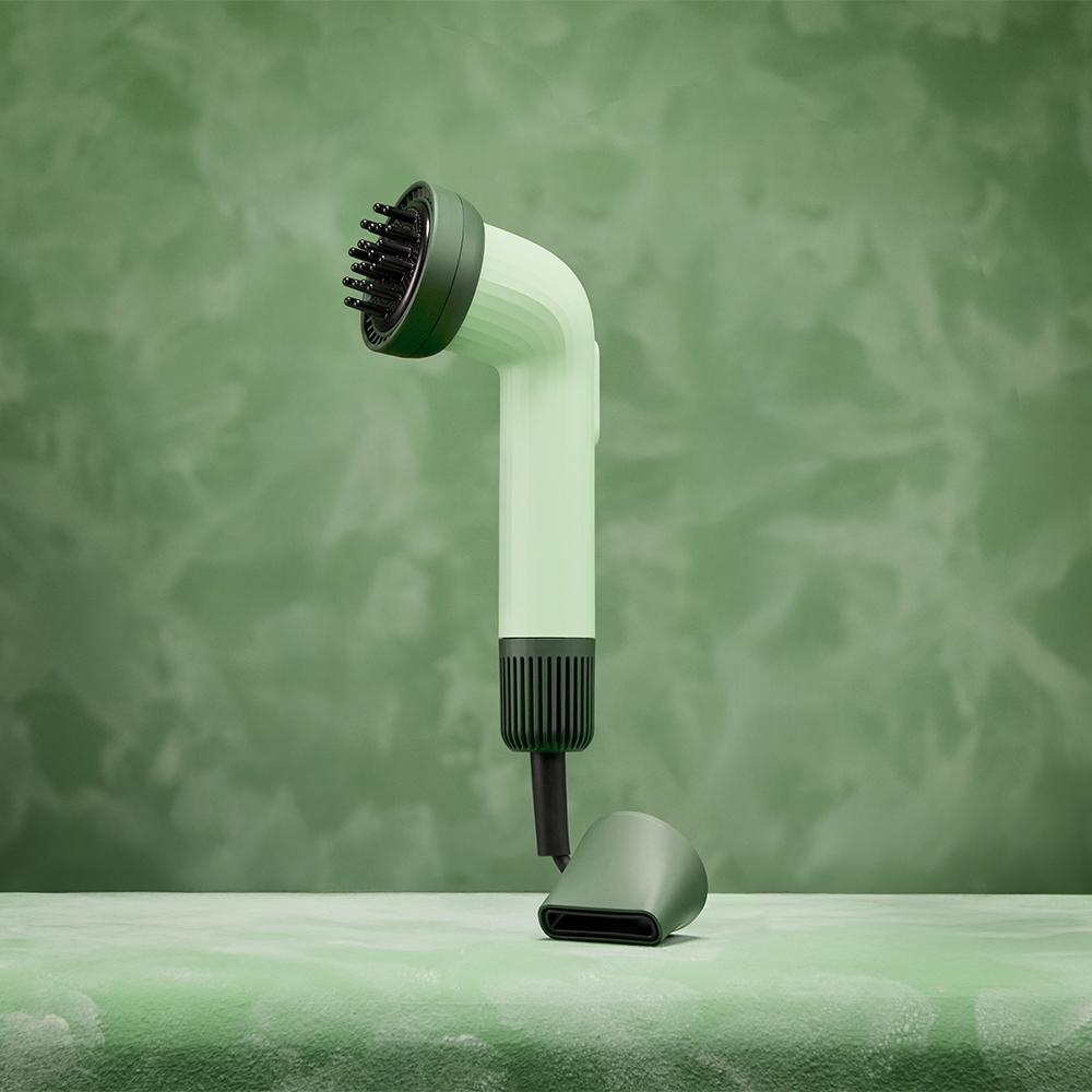 Un secador de pelo con cuerpo verde y detalles verde oscuro. Se encuentra sobre una superficie verde, contra un fondo verde texturizado.