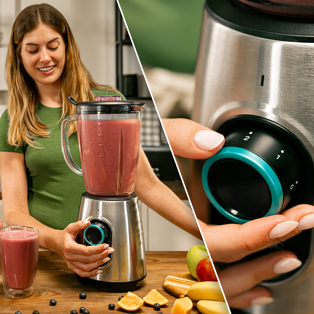 Una mujer usa una licuadora para hacer un batido. La licuadora es plateada con un tarro de vidrio. Frutas y un vaso de batido están en la mesa.