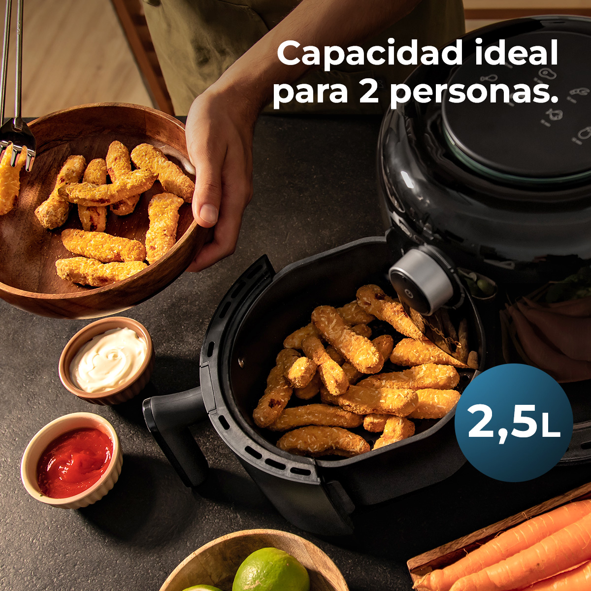 Una freidora de aire con alimentos fritos, salsas y verduras. Una persona sostiene un cuenco con alimentos fritos. Capacidad ideal para 2 personas.