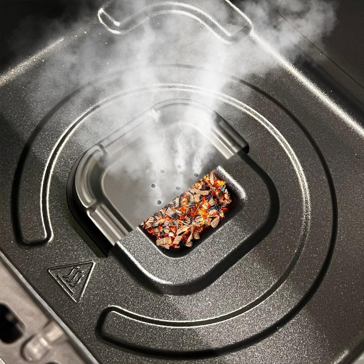 Primer plano de una parrilla humeante. Se ven astillas de madera ardiendo. El vapor se eleva. La parrilla es gris oscuro.