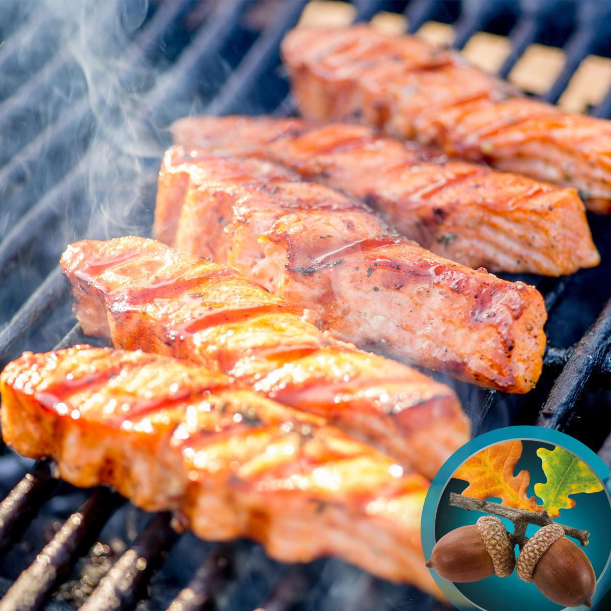 Filetes de salmón a la parrilla en una barbacoa, con humo ascendente. Bellotas y hojas en el fondo.