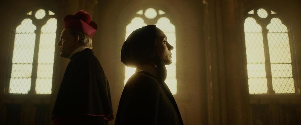 Zwei Personen in religiöser Kleidung stehen in der Nähe von Bogenfenstern. Die Frau ist im Profil. Der Mann trägt einen roten Hut.