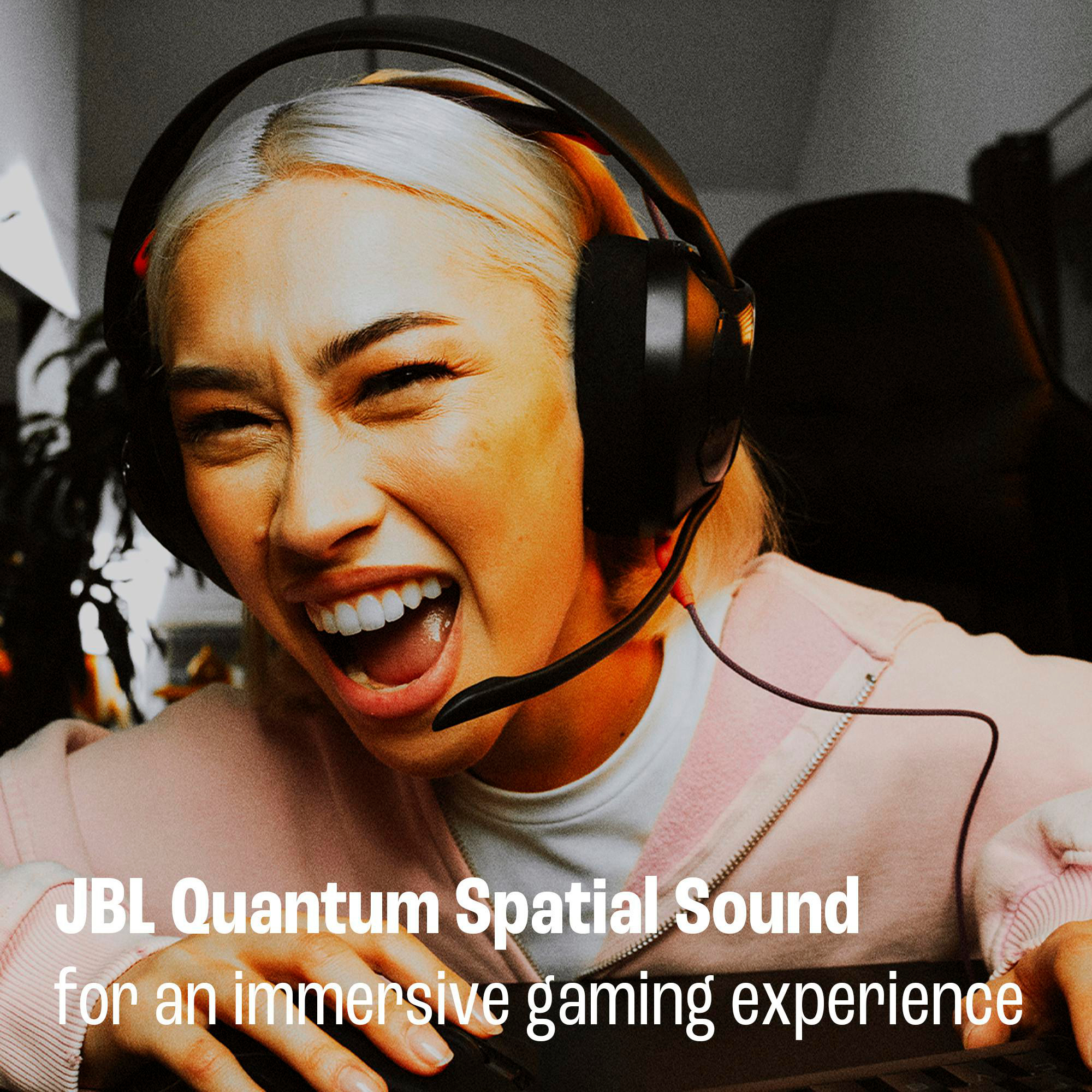 Frau mit Kopfhörern, spielt, lächelt breit. JBL Quantum Spatial Sound Text steht unten.