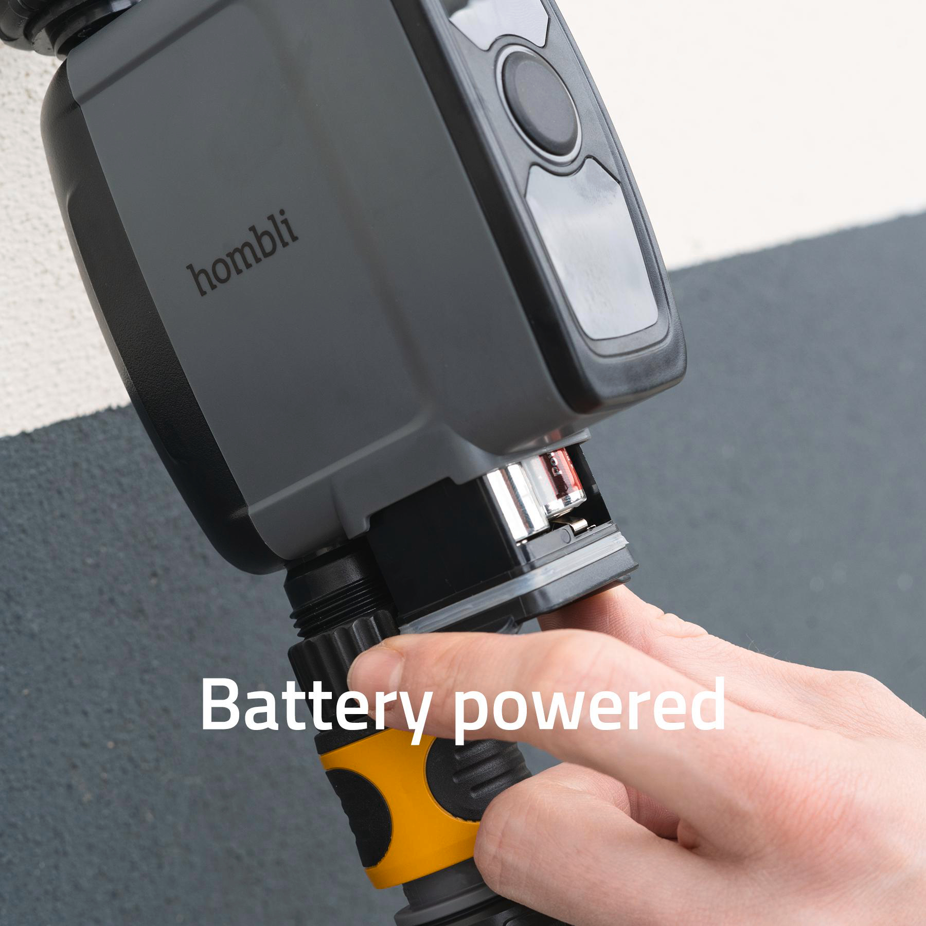 Ein graues Gerät mit dem Wort 'hombl' wird gehalten. Ein Finger öffnet das Batteriefach. Text: Batteriebetrieben.