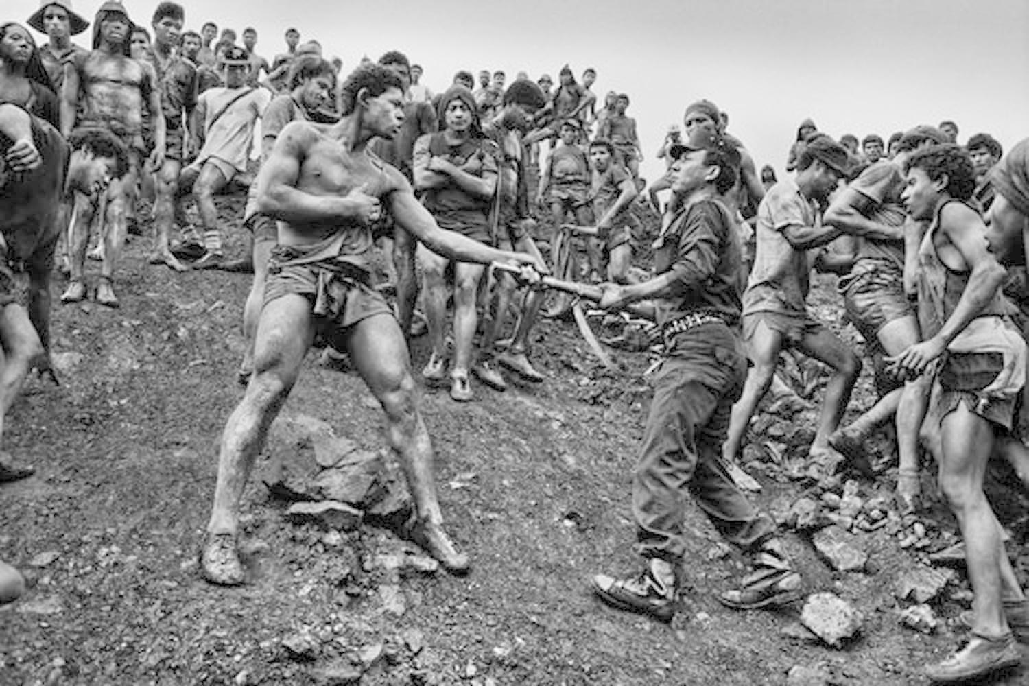 Bergleute kämpfen um ein Werkzeug. Männer in Shorts und Hemden, bedeckt mit Schmutz, umgeben von einer Menschenmenge auf einem schlammigen Hügel, kämpfen.