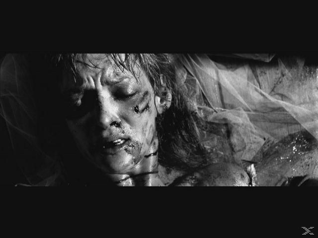 Eine verstörte Frau mit Blut im Gesicht liegt. Sie scheint Schmerzen zu haben, mit einem Tuch, das einen Teil ihres Körpers bedeckt.